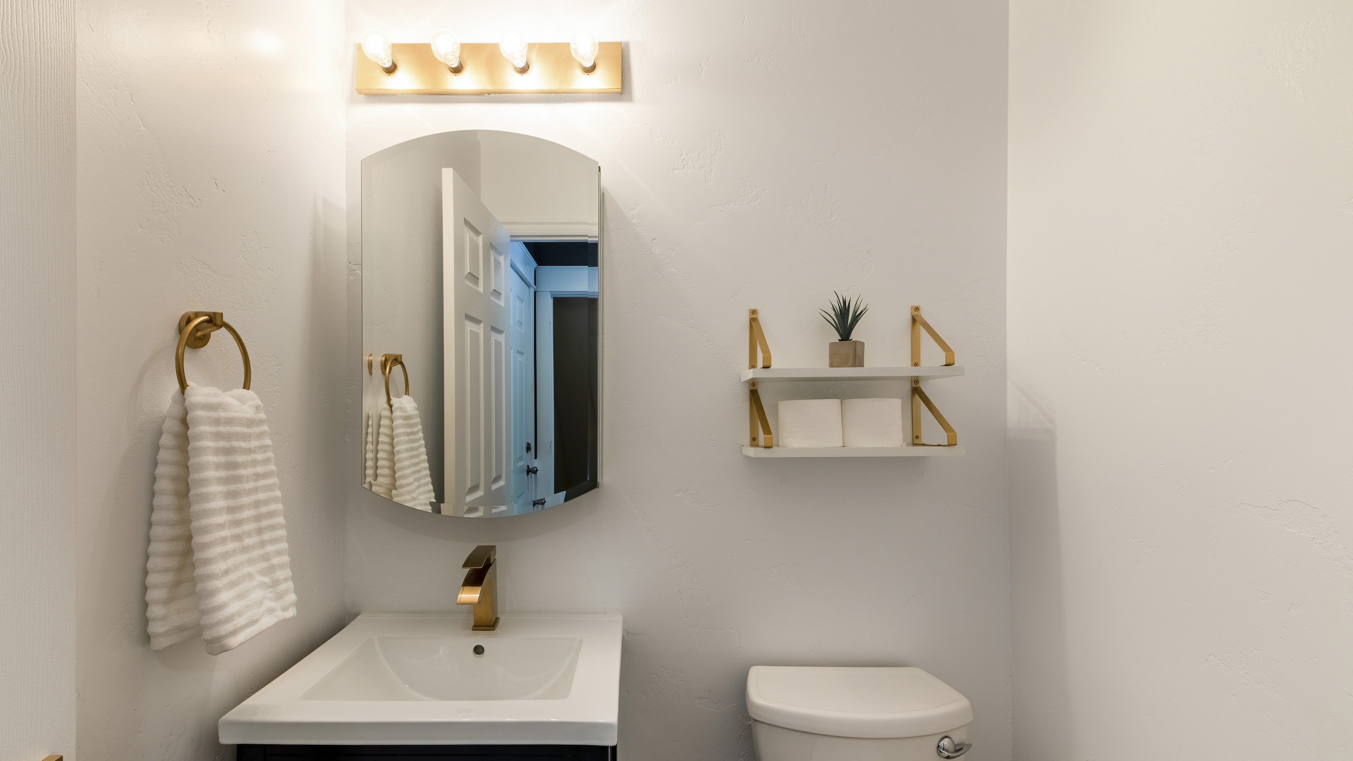 Small powder room with matching gold faucet, towel ring, and open-concept shelf 