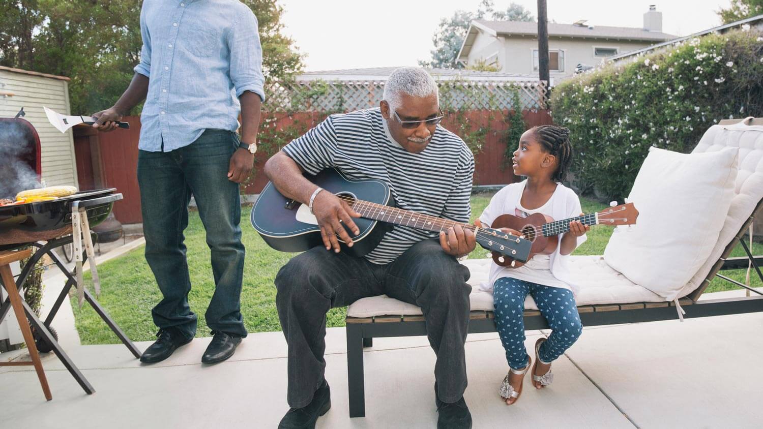 A grandfather and his granddaughter playing guitar in their patio