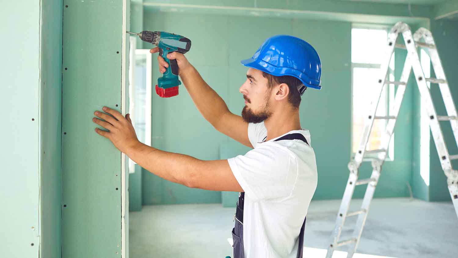 Worker installing green drywall in a new construction