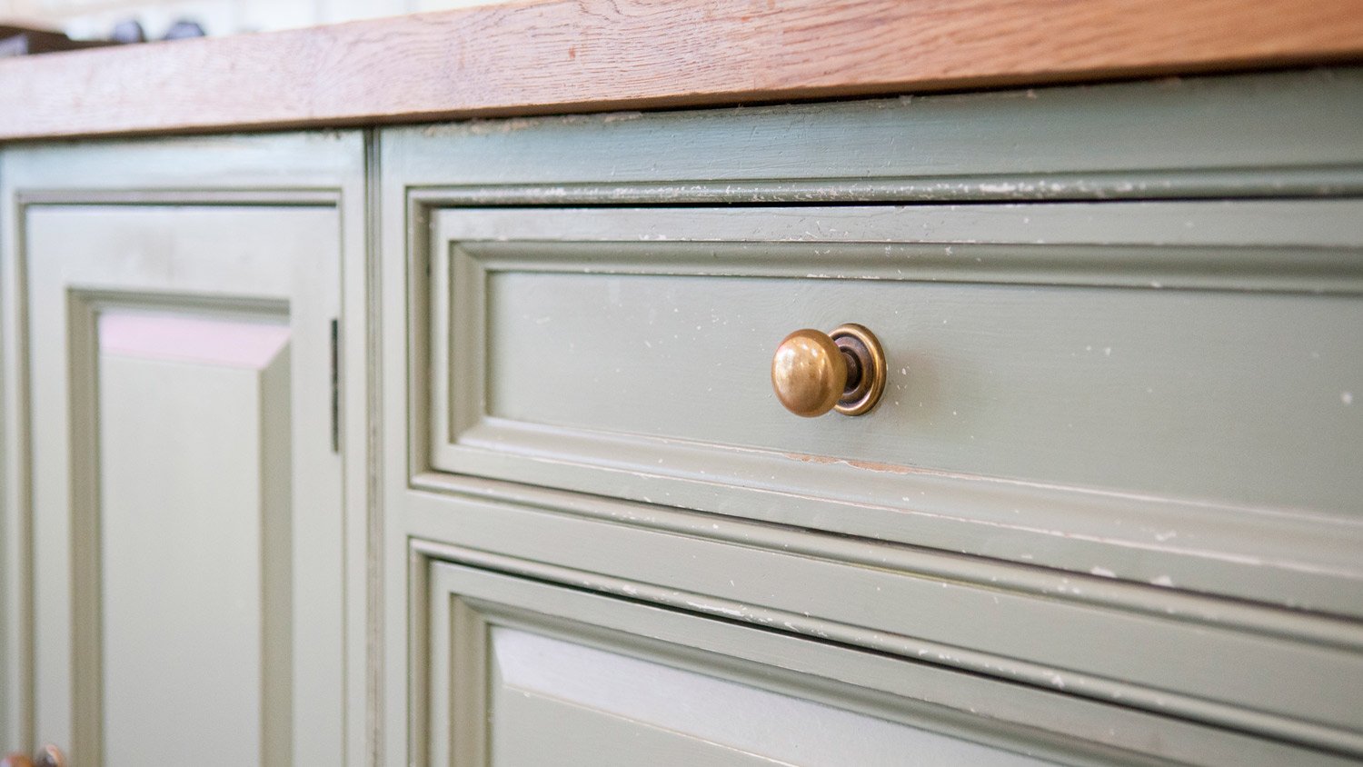 A close up detail of a green kitchen drawer with a brass knob