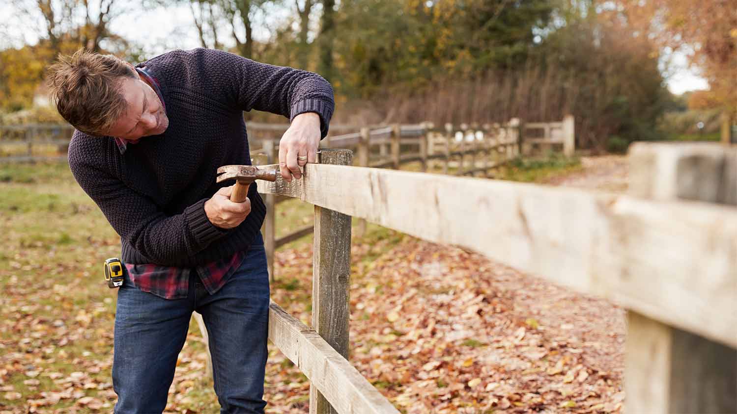 man hammering nail into fence post