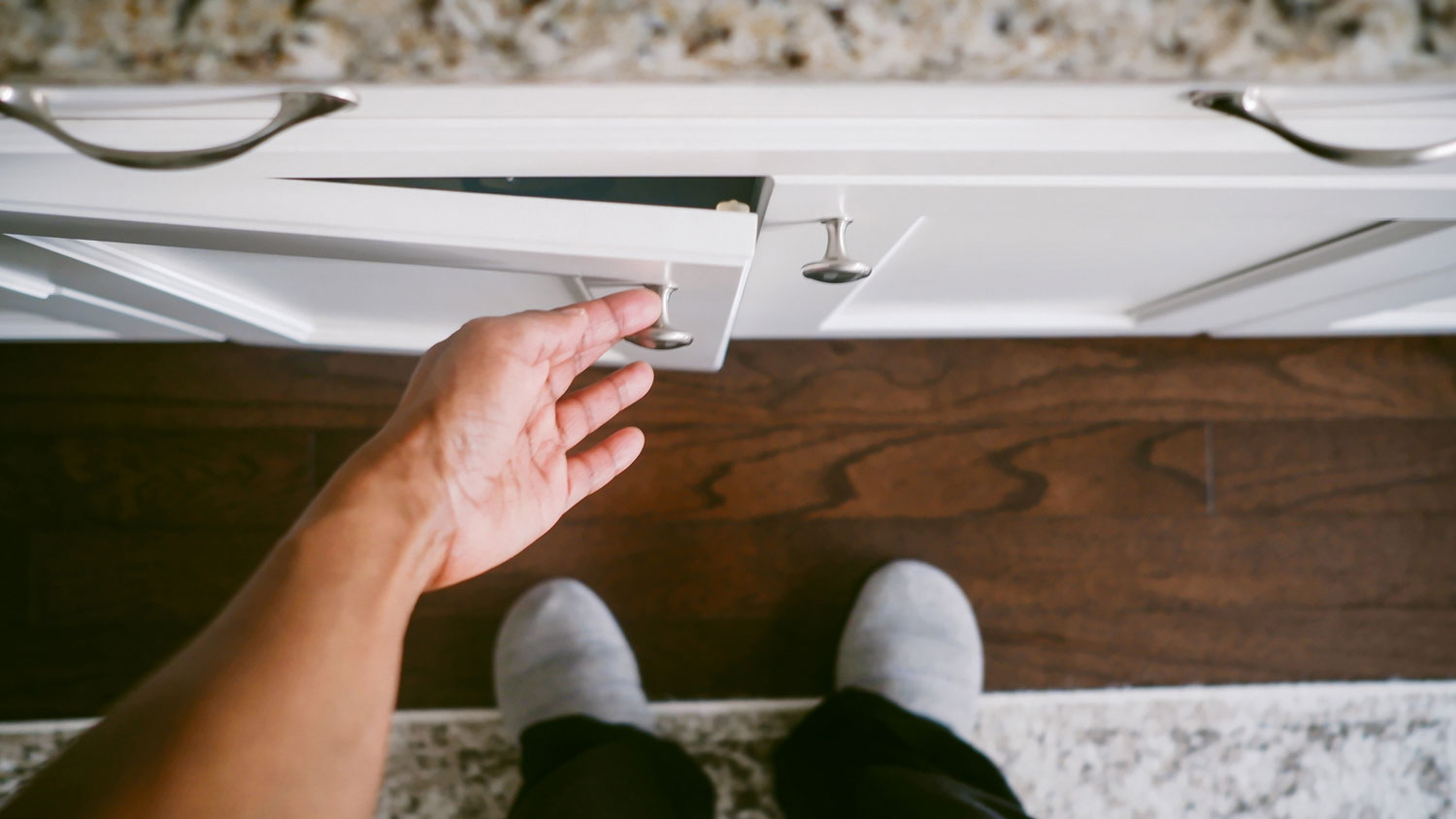 A hand opening a cabinet by the knob