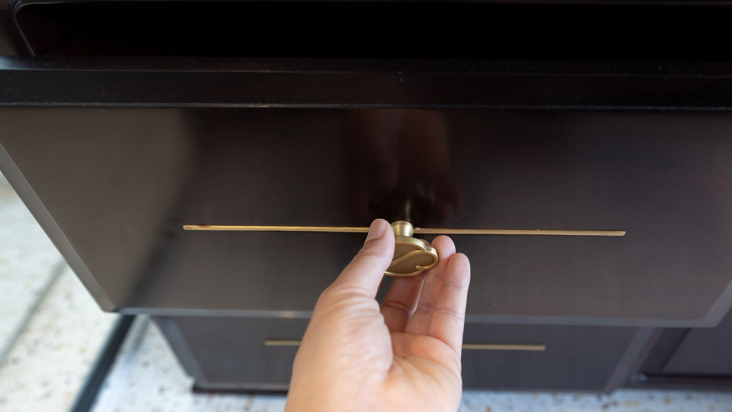 A hand pulling a cabinet with a knob and a minimal backplate