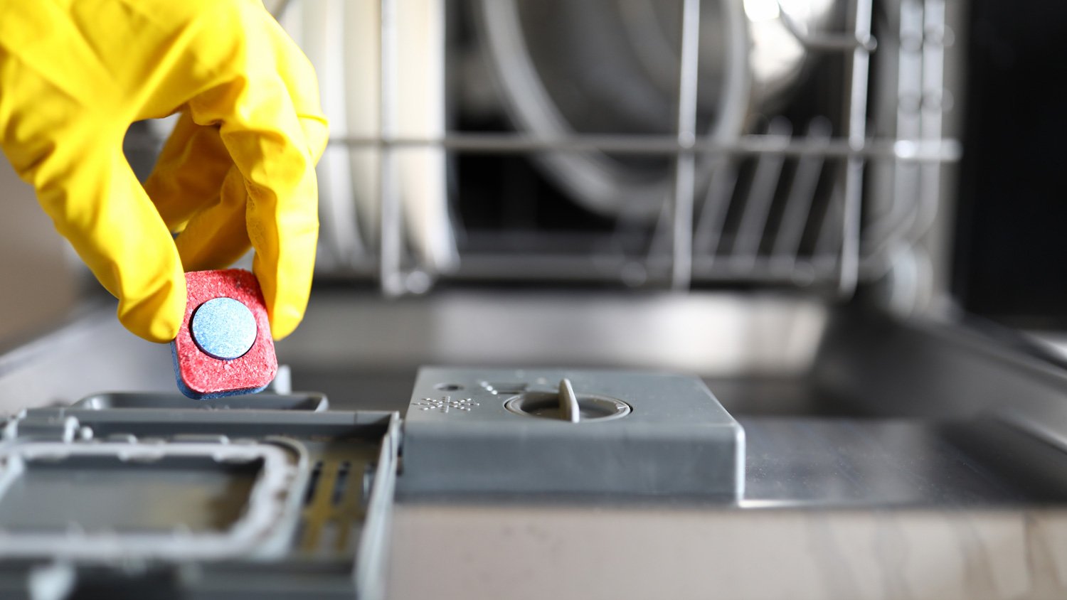 Close-up of a hand in glove putting capsule in dishwasher