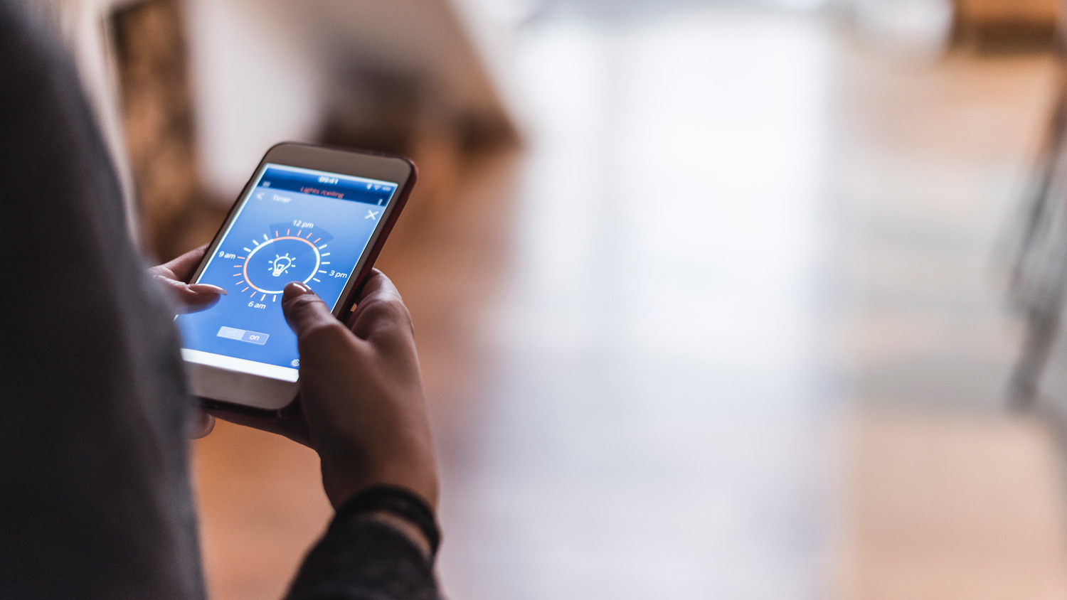 A woman’s hand using a smartphone controlling her smart home