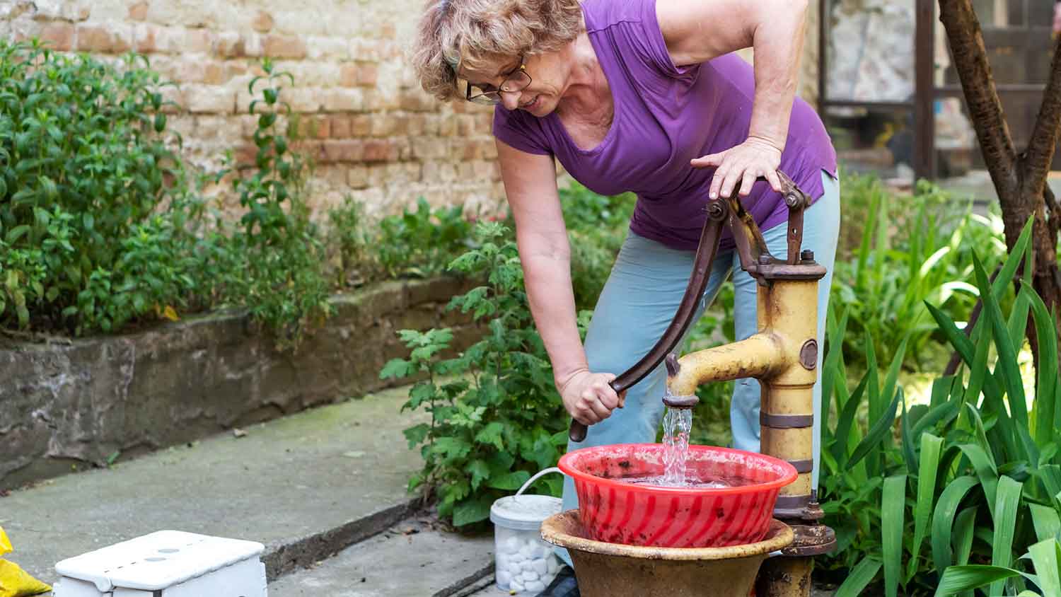 Woman using hand pump to draw water from the well