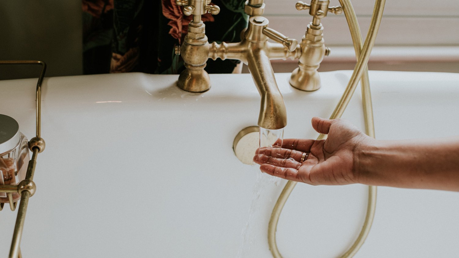A woman checks the temperature of bath water by holding her hand under the faucet
