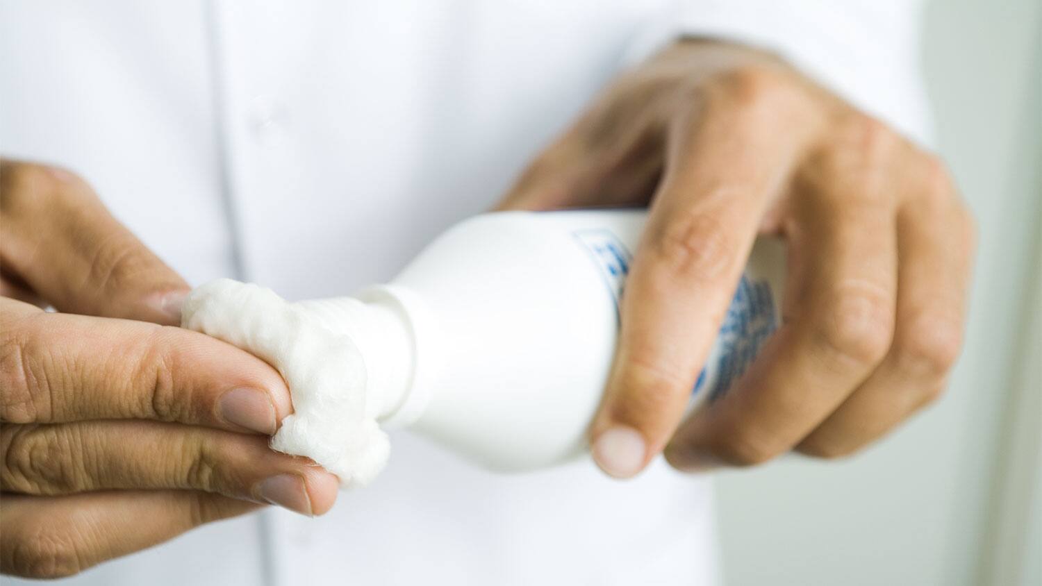 Hands putting rubbing alcohol on cotton ball