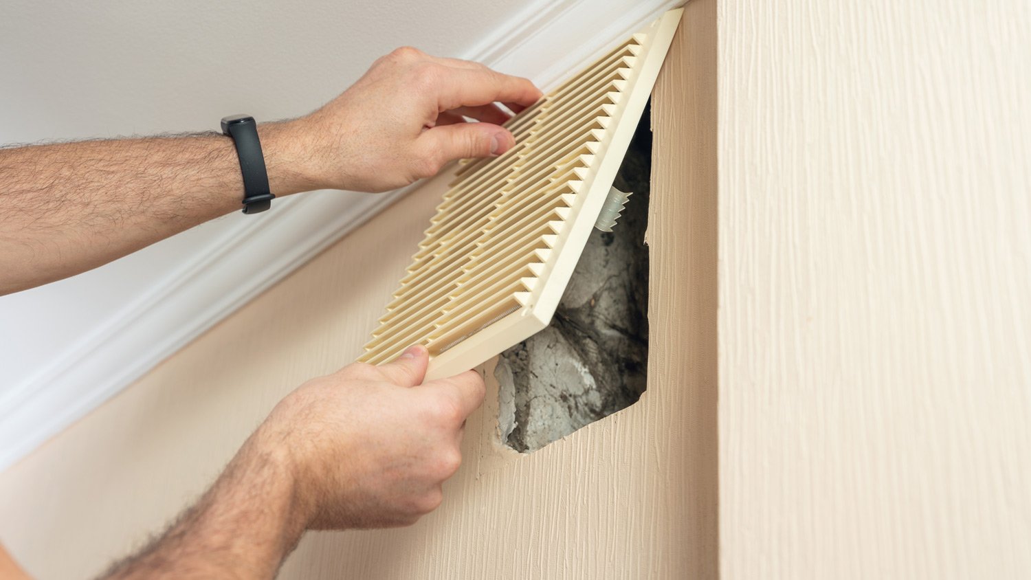 A man removes a plastic ventilation grille for later cleaning