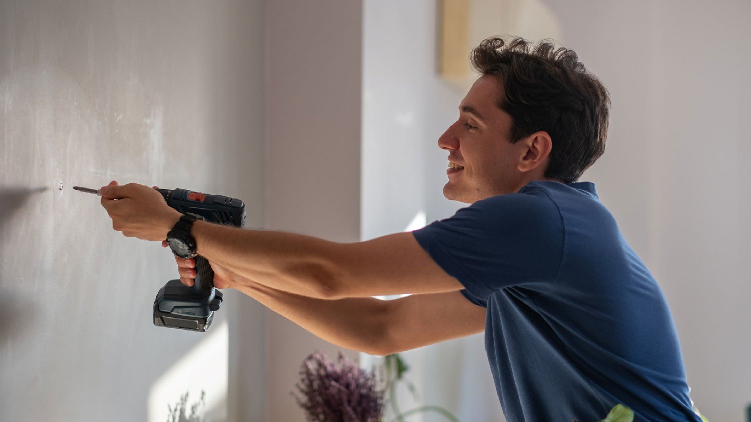 A handyman using a drill to screw in a drywall