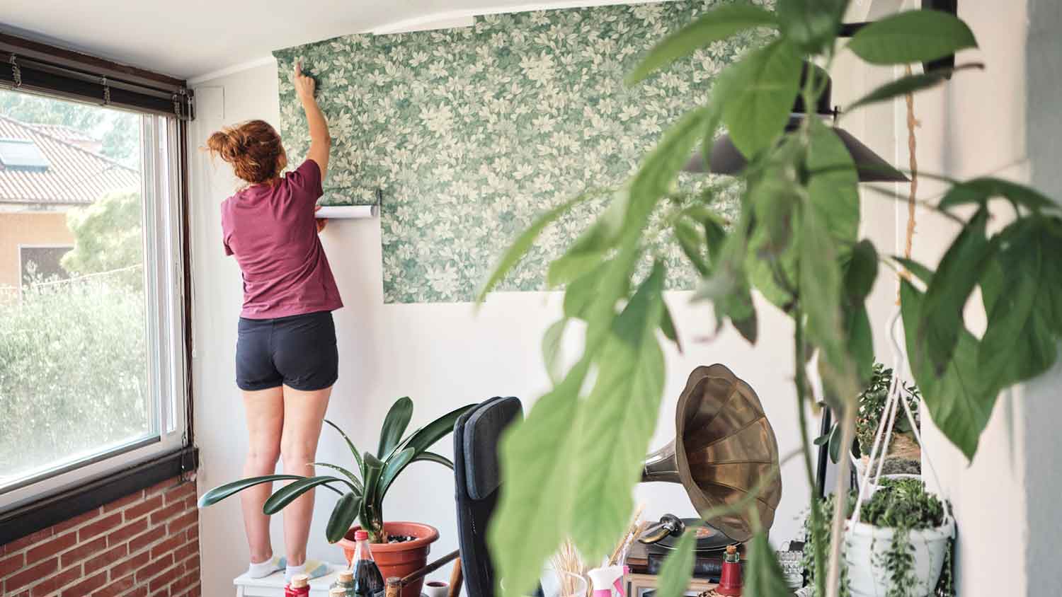 Woman hanging vinyl wallpaper in the room