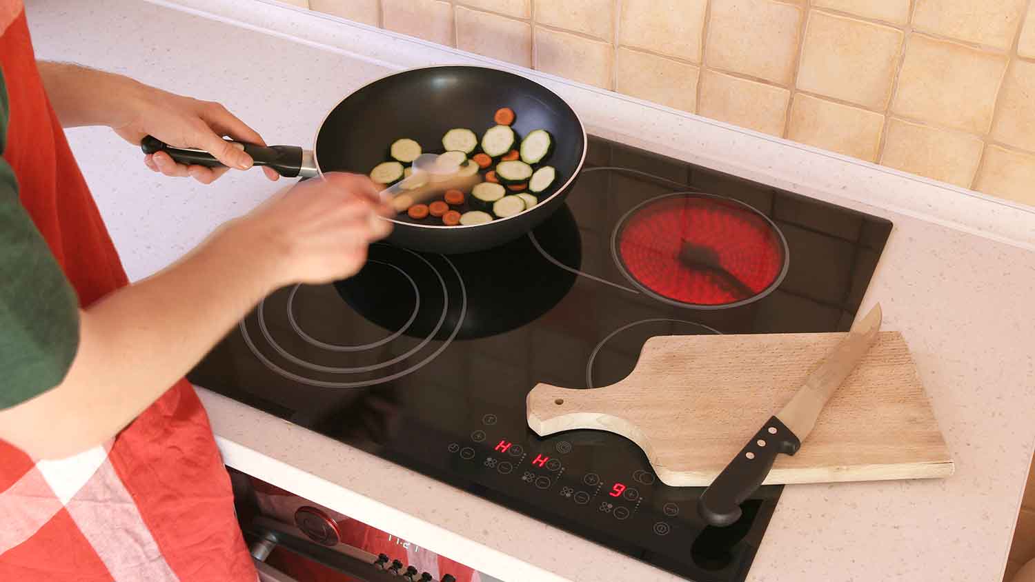 Person cooking veggies on a glass cooktop 