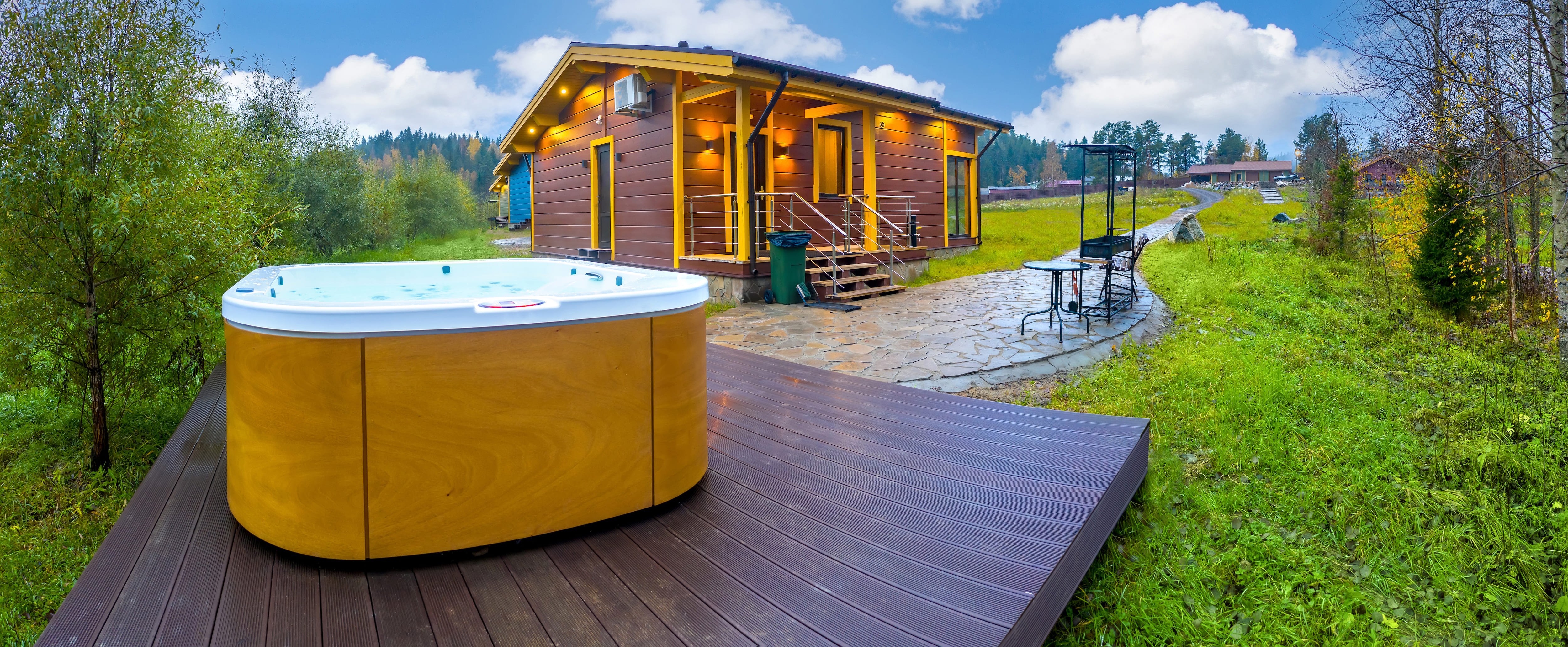  small home with a stone patio leading into a small wooden deck with a hot tub on top