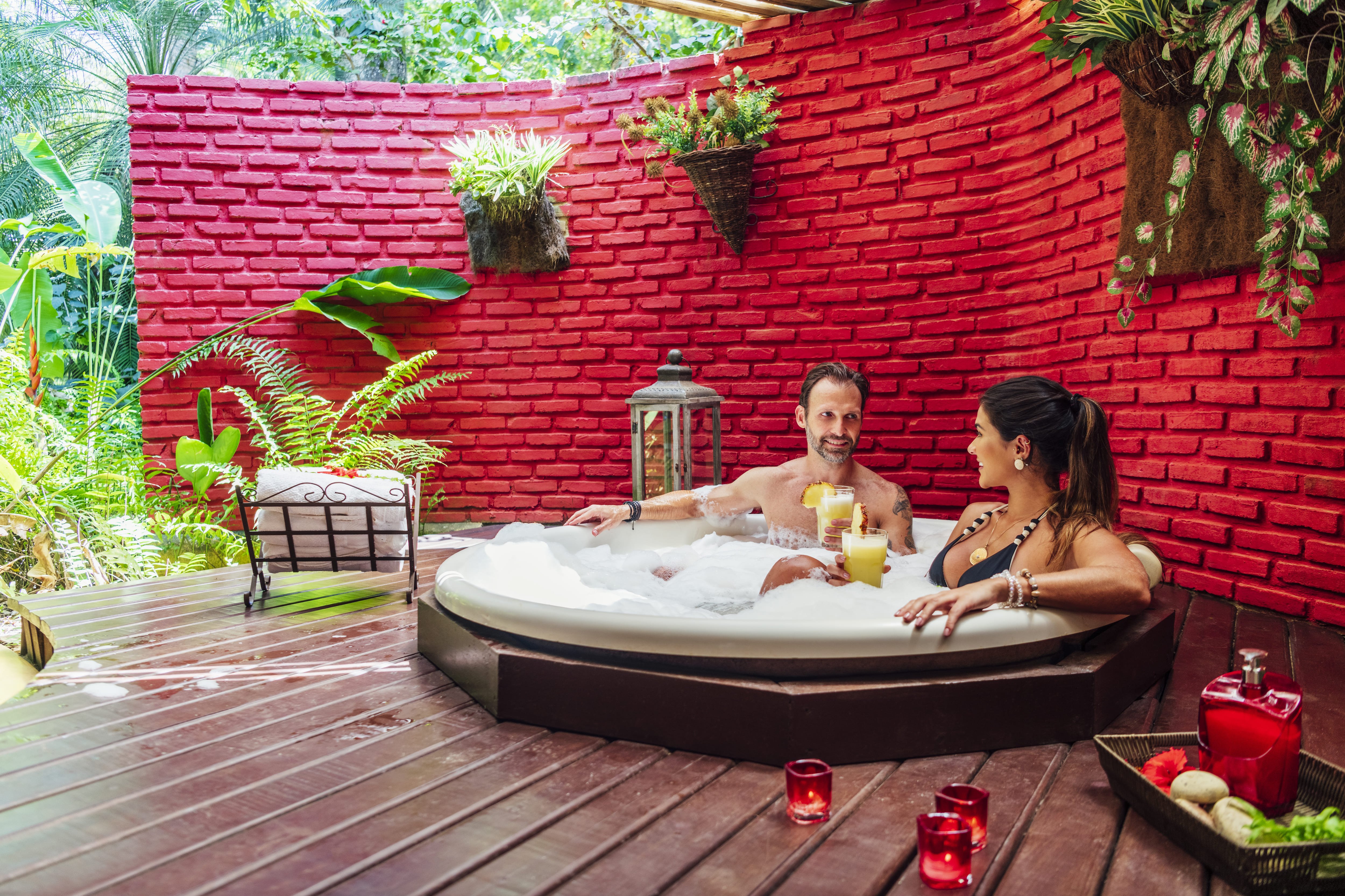 A couple sits in a hot tub shielded by a faux brick privacy wall