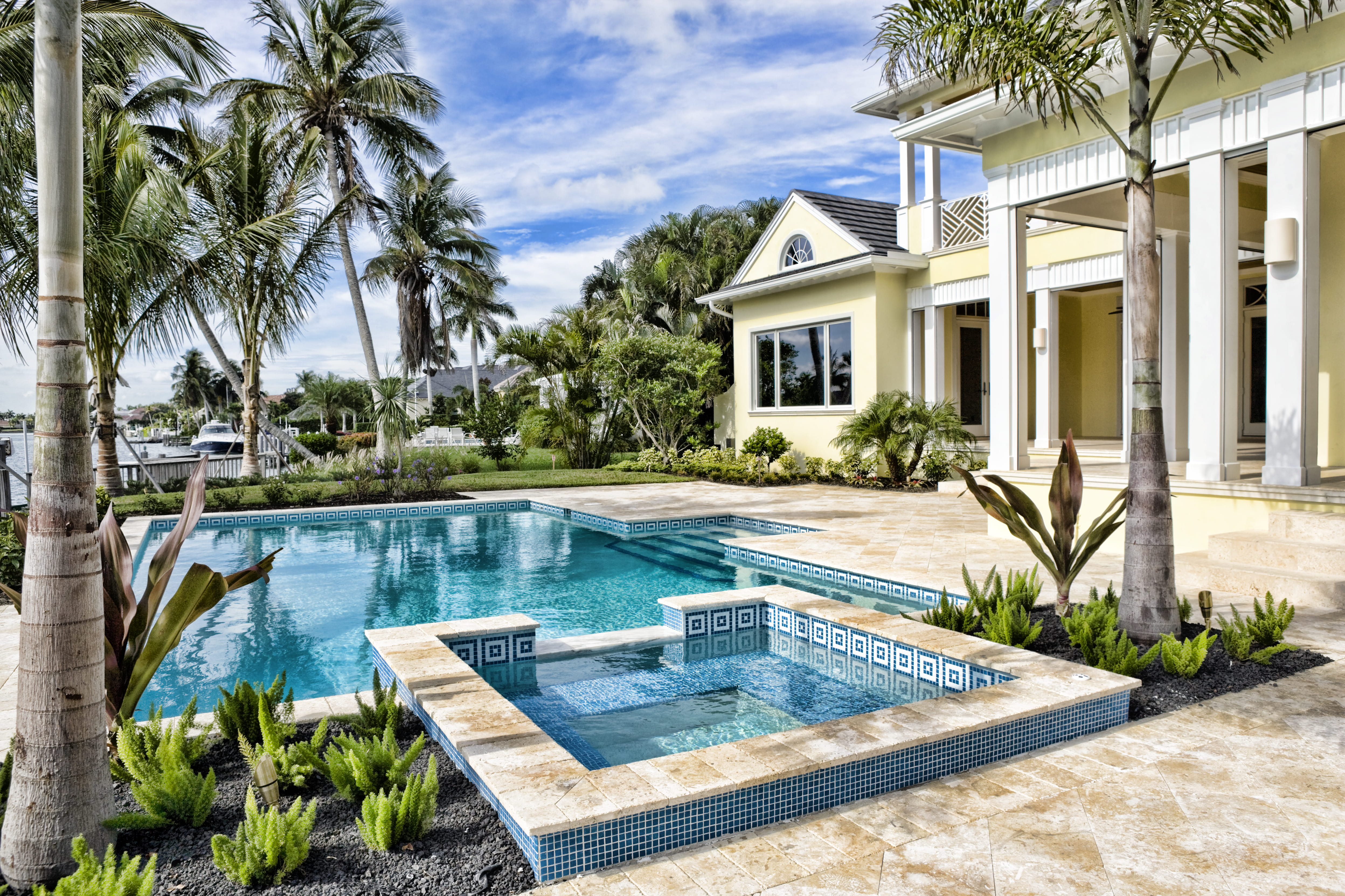 A tropical looking backyard with a hot tub lined with tile on its interior and exterior