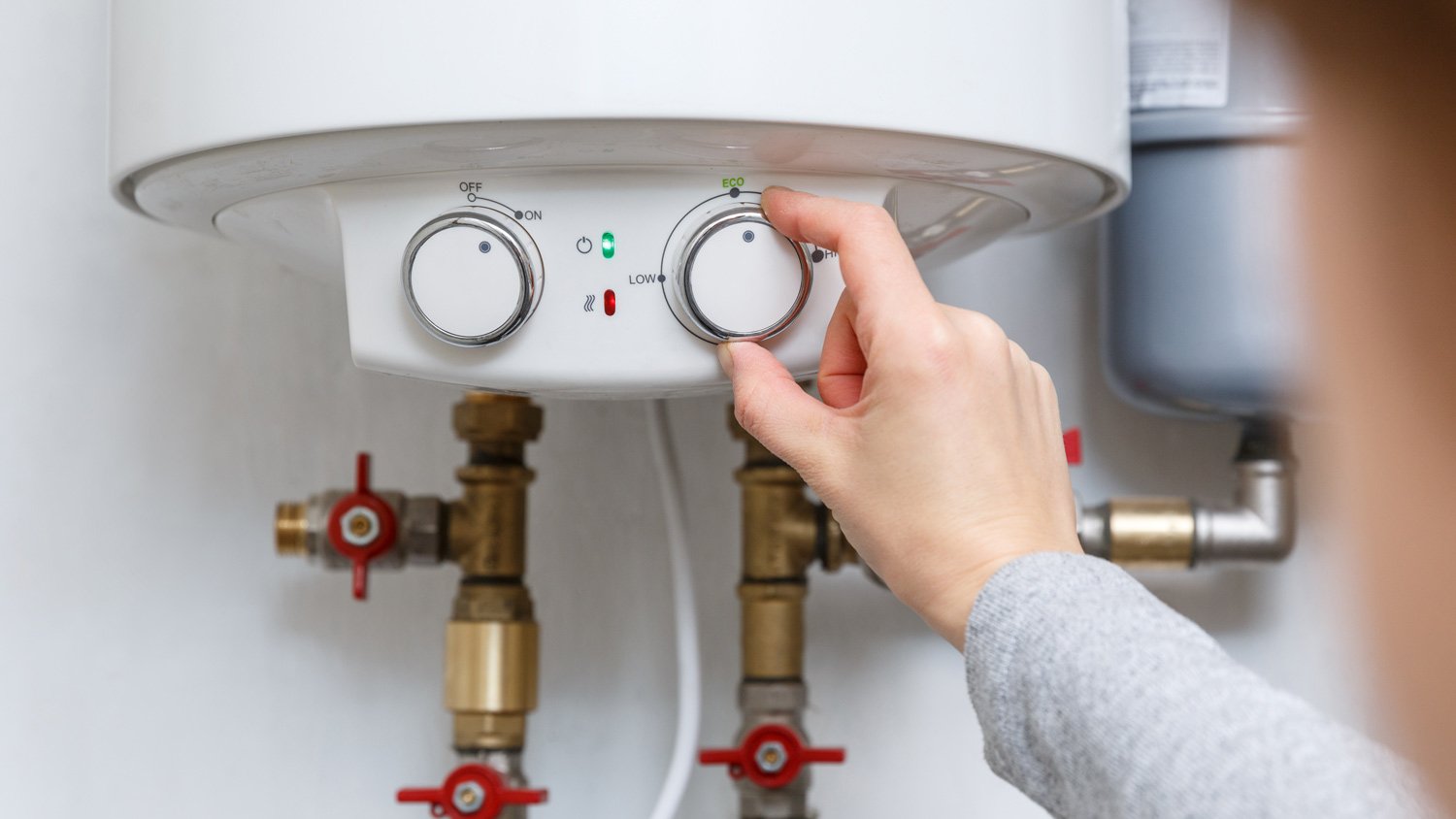 Female hand puts thermostat of electric water heater