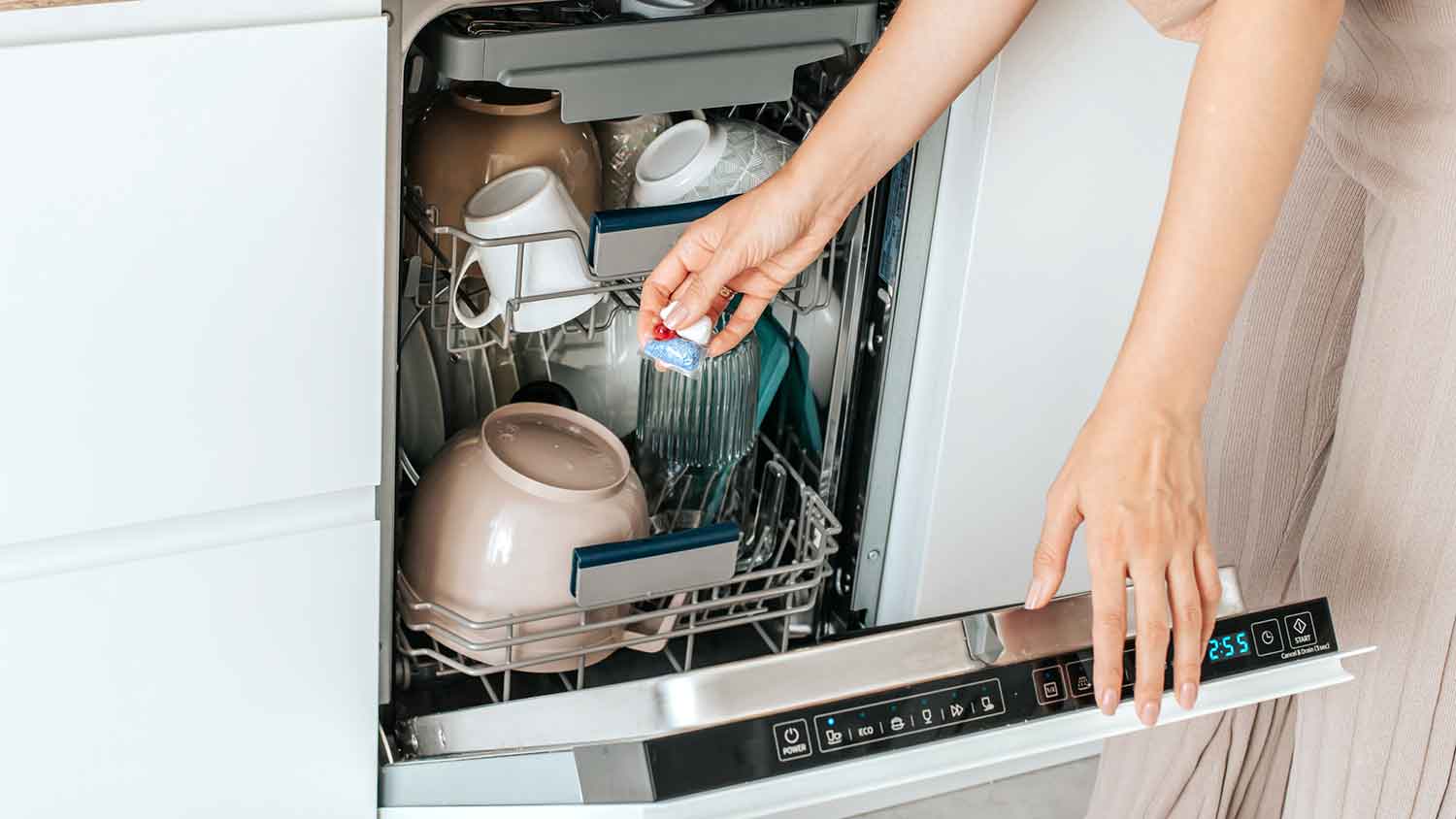 A person adding a dishwasher pod to a dishwasher full of dirty dishes