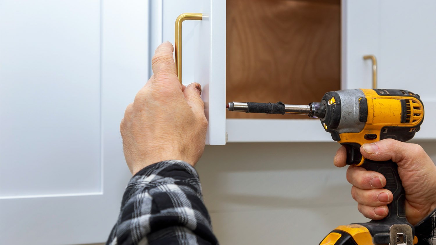 man installing gold handle on white cabinet