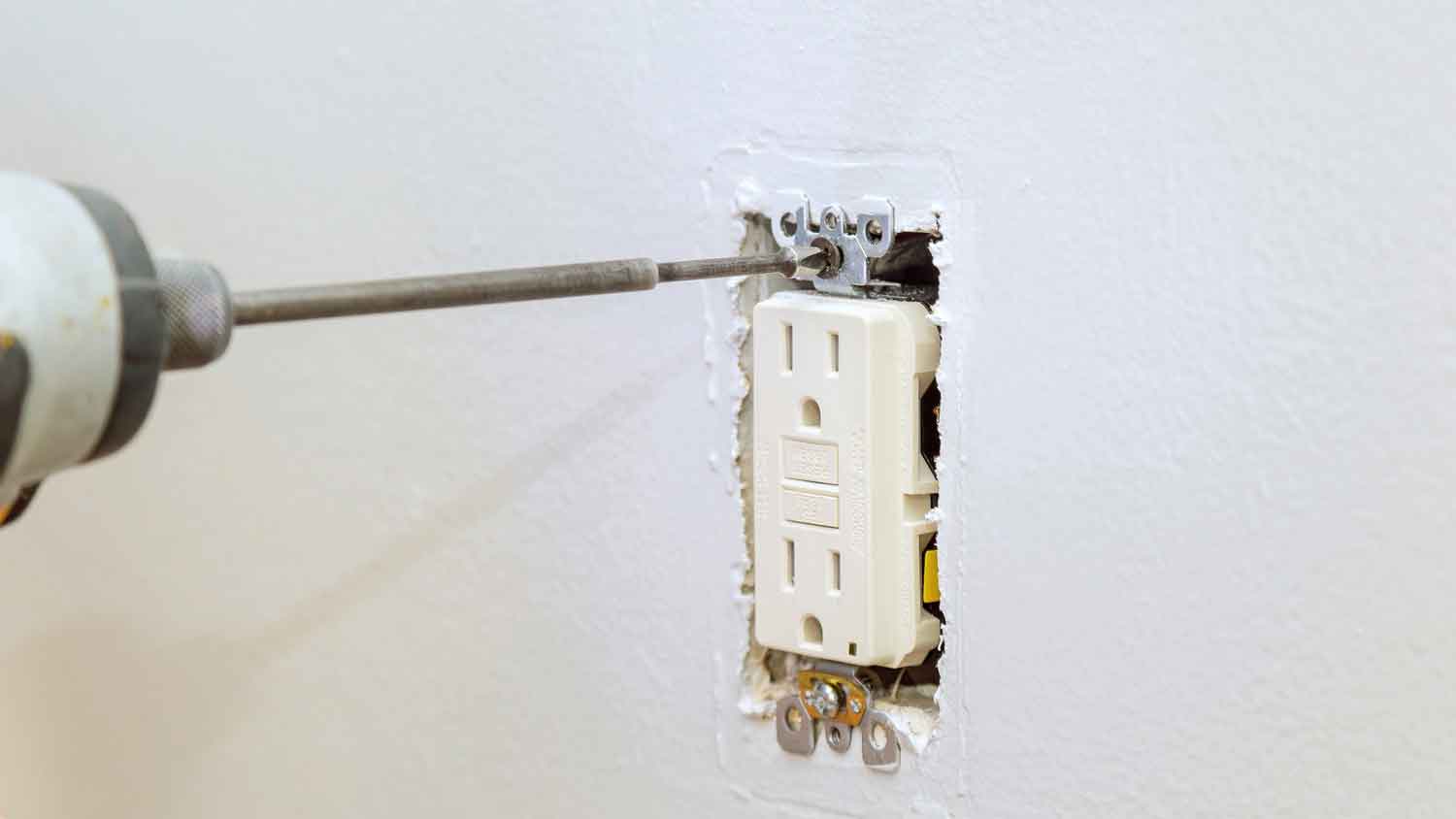 Using electric screwdriver to install GFCI outlet on the wall