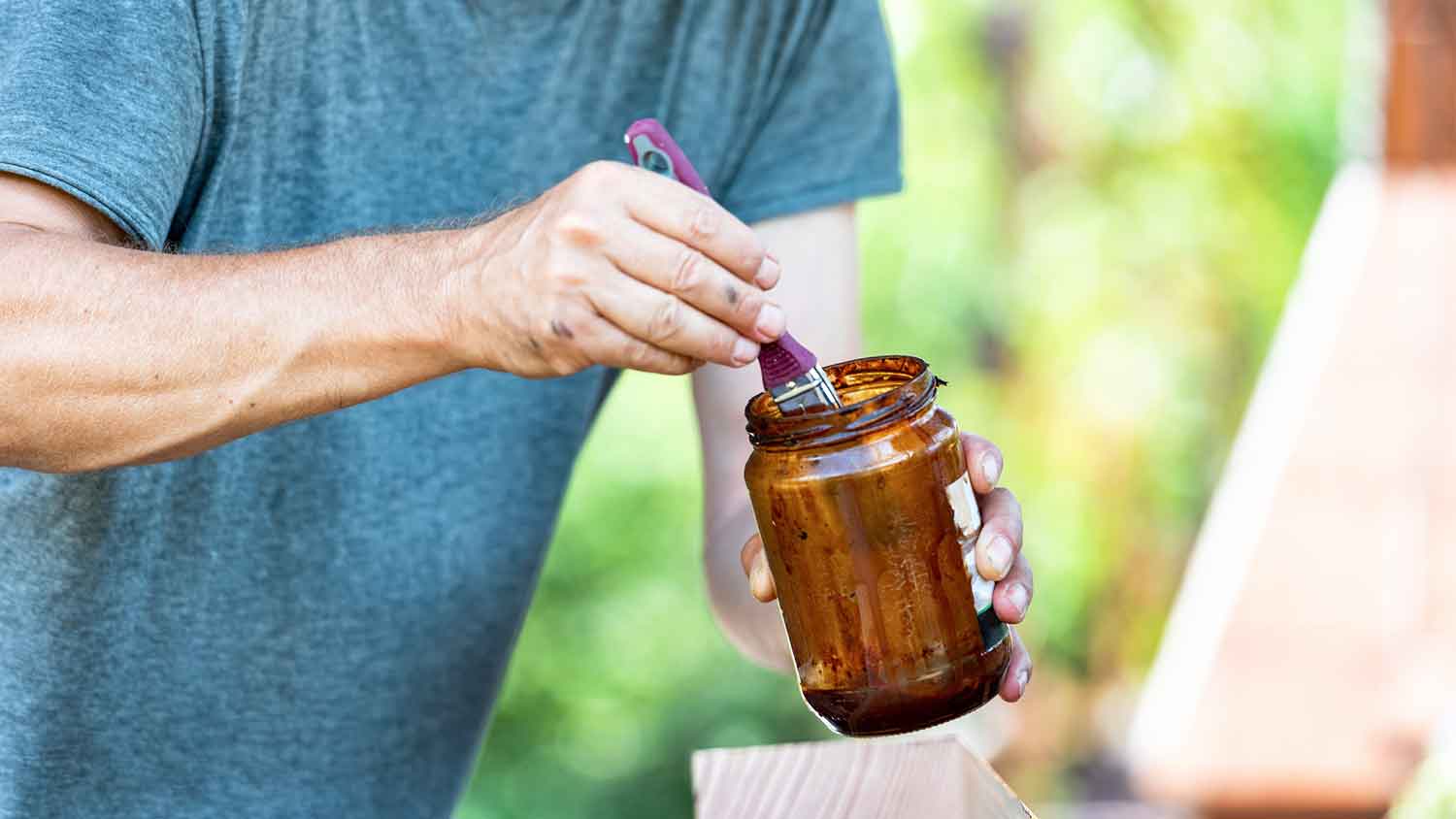 Man dipping a brush in a jar with wood stain