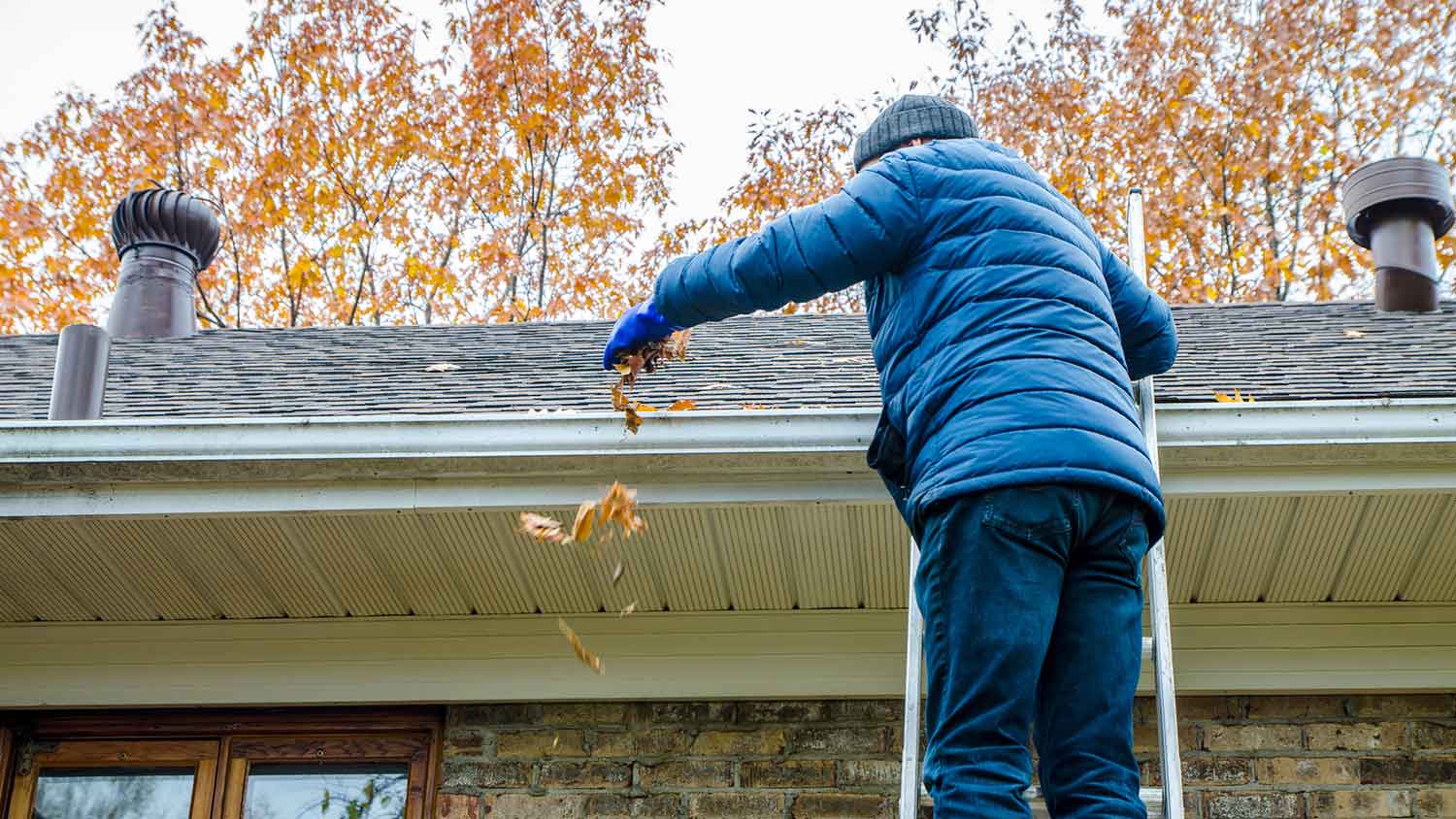 Man in a ladder removing autumn leaves from gutter