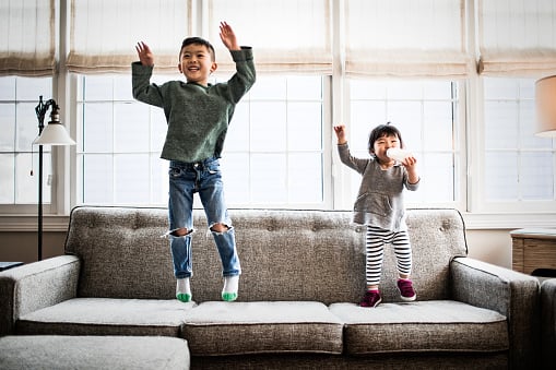Siblings jumping on a couch at home
