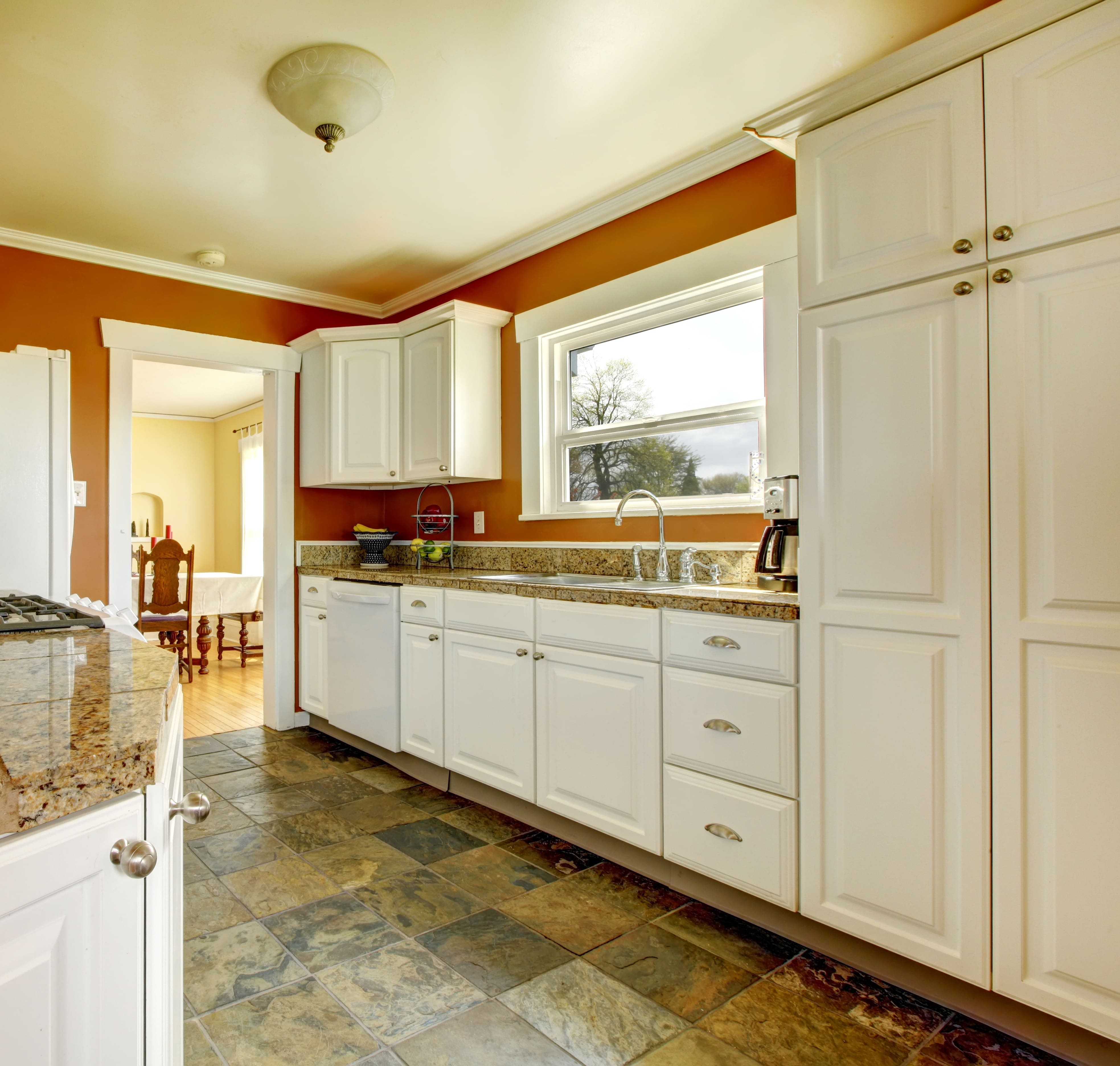 A side image of a kitchen with burnt orange walls and soft white cabinets