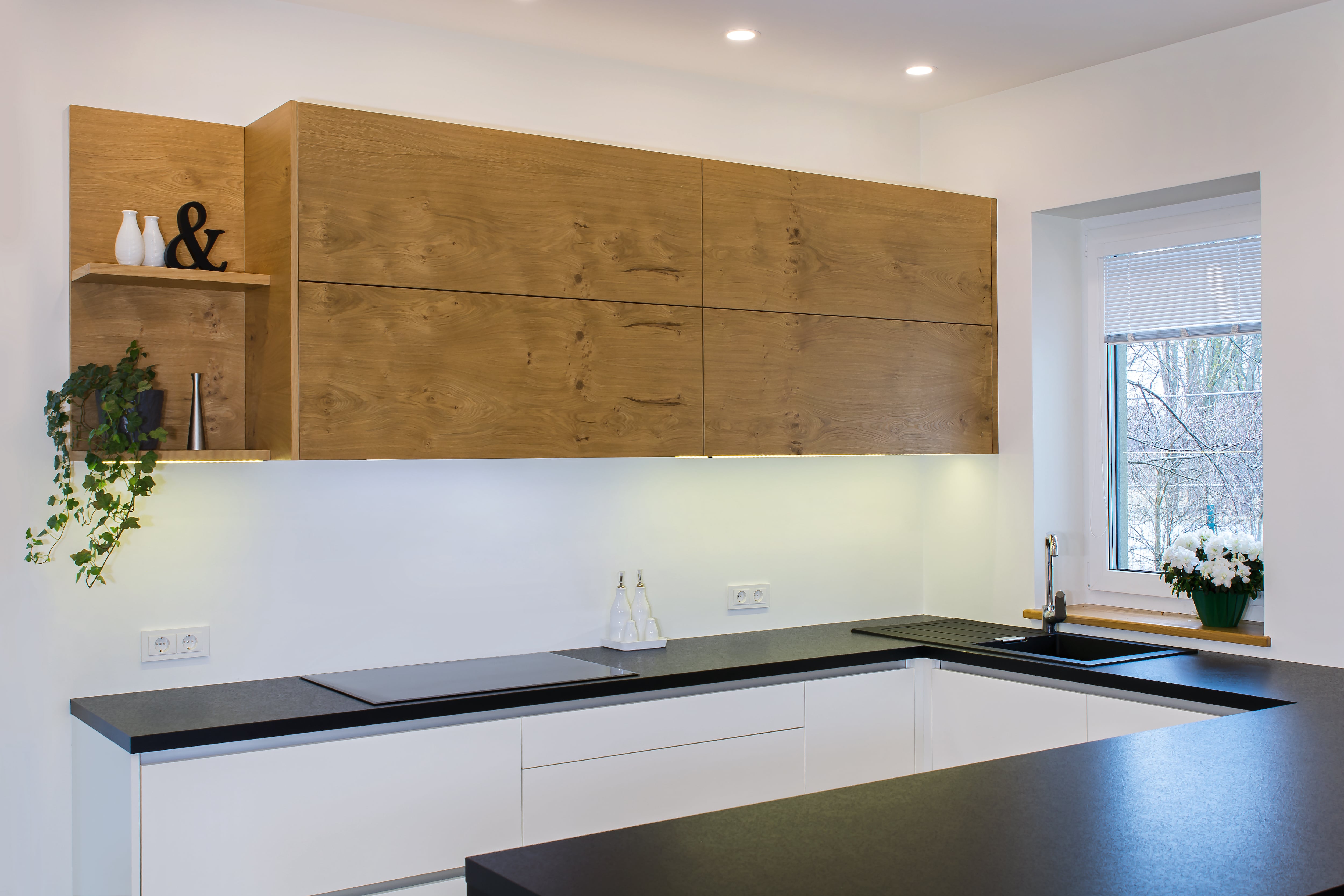Modern European kitchen with black laminate countertops, white cabinets and wood cabinets, and white walls