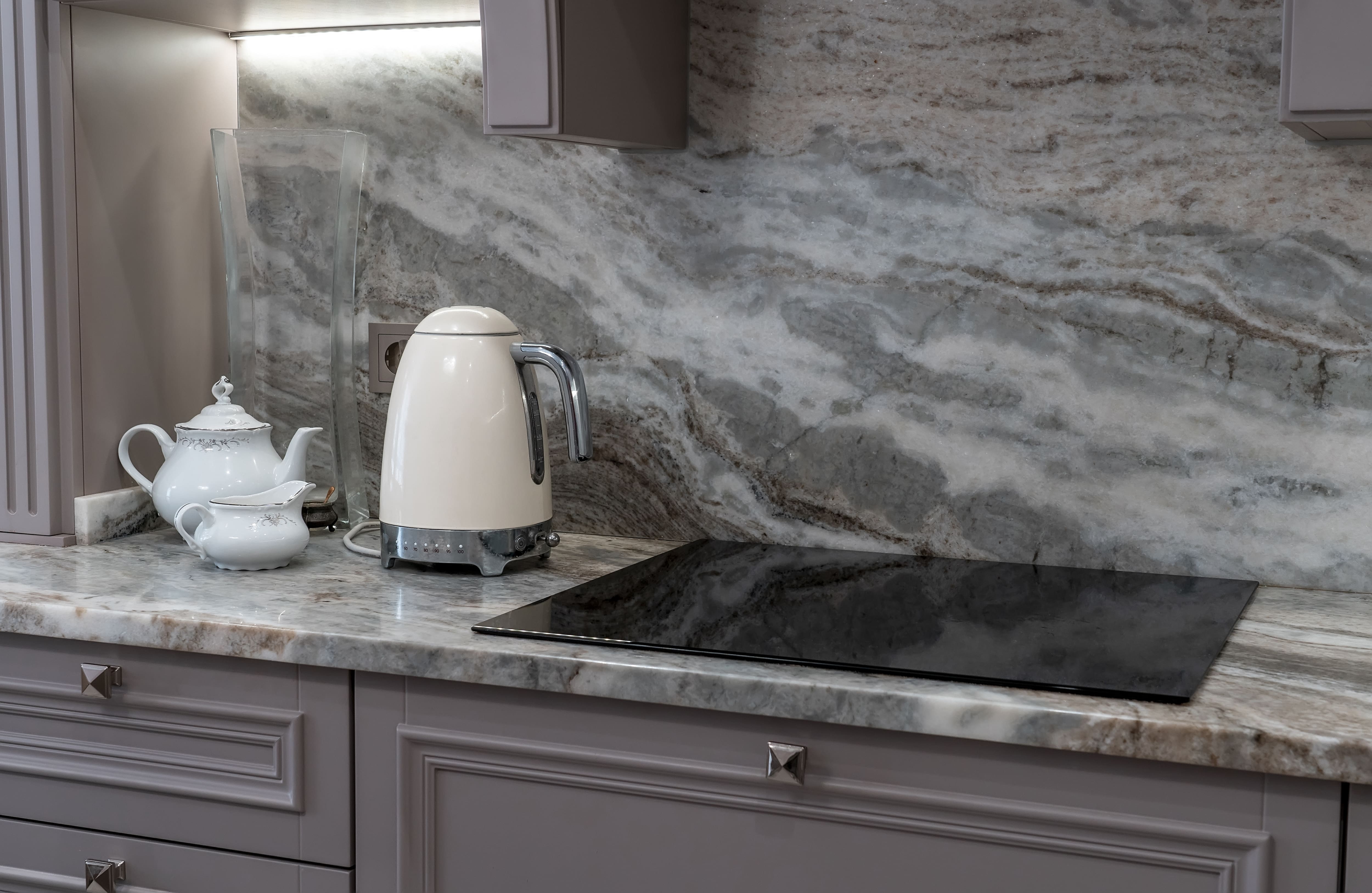 Kitchen with dark quartz countertop and backsplash with gray and gold veins, gray cabinets, and white tea pot and kettle