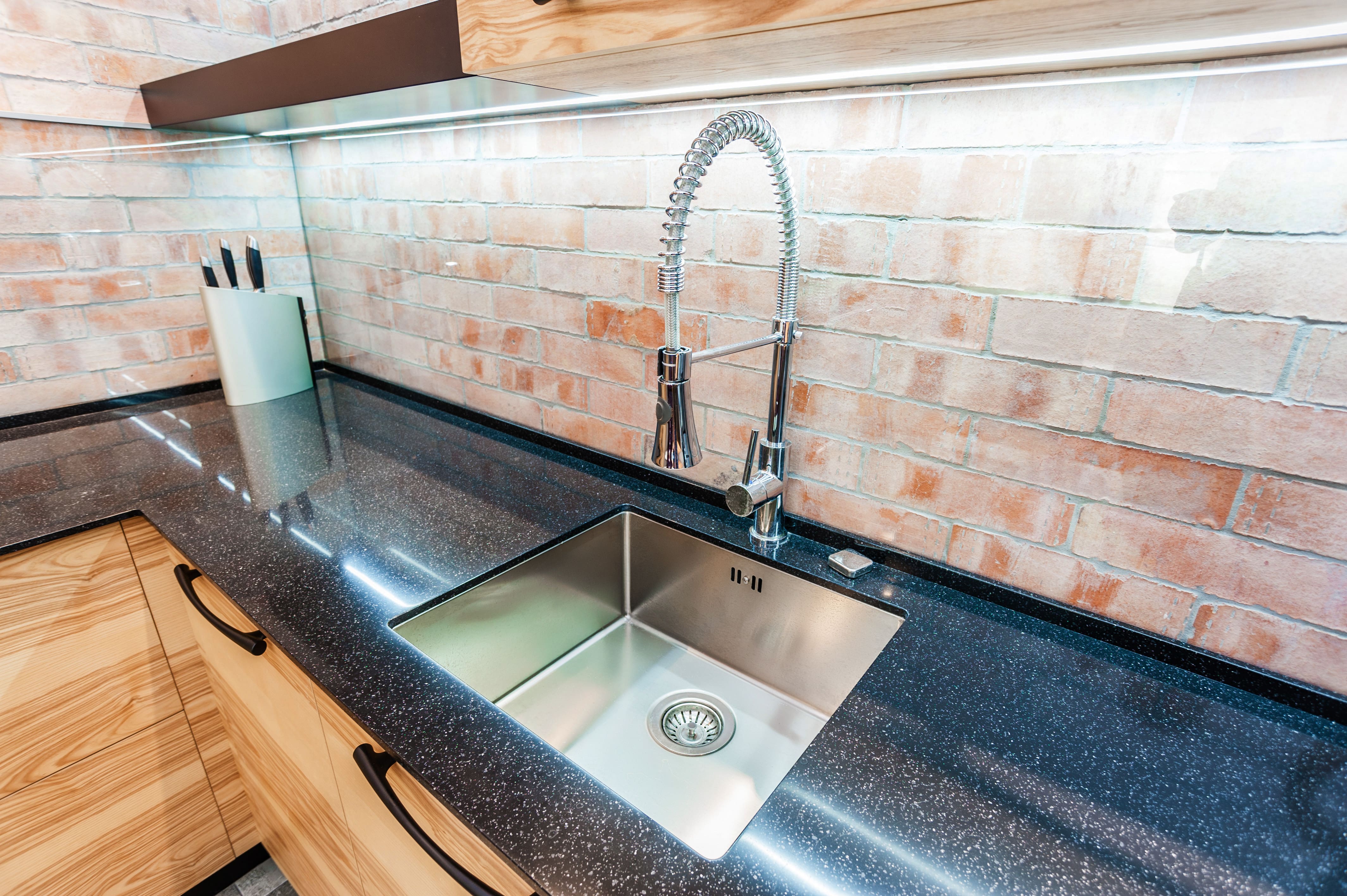 Modern kitchen with black recycled glass countertops, brick backsplash, wood cabinets, and chrome sink