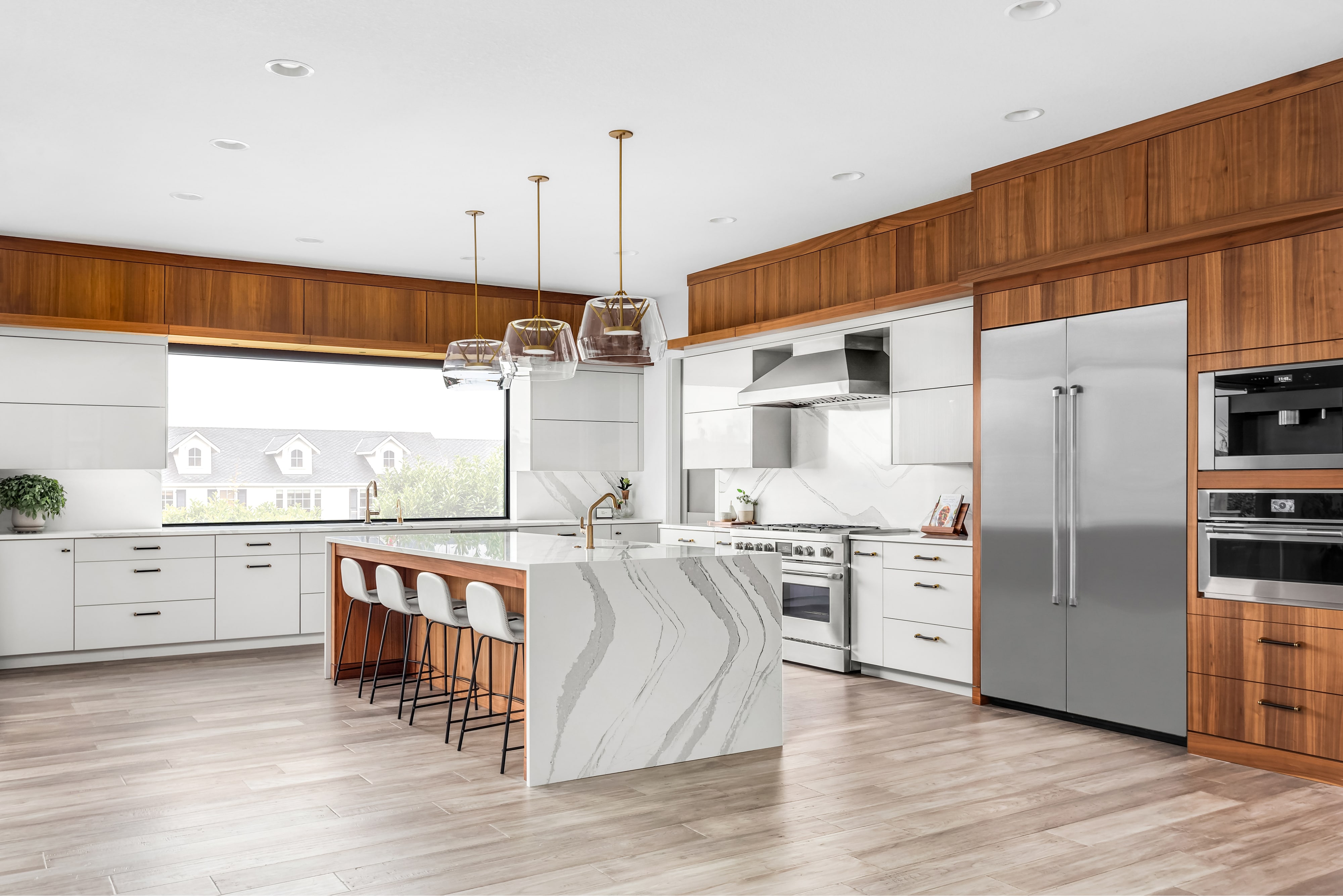 Luxury kitchen with large marble waterfall island, marble backsplash, and white and wood cabinets