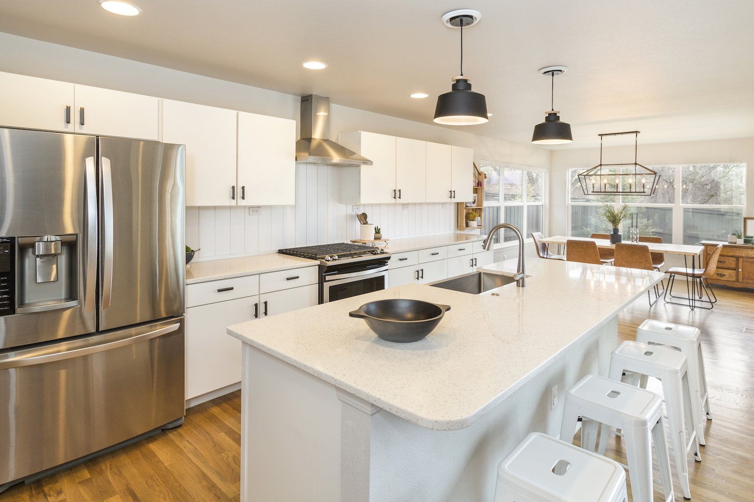 Modern farmhouse kitchen with big center island, white cabinets, countertops and shiplap backsplash, and wood kitchen table