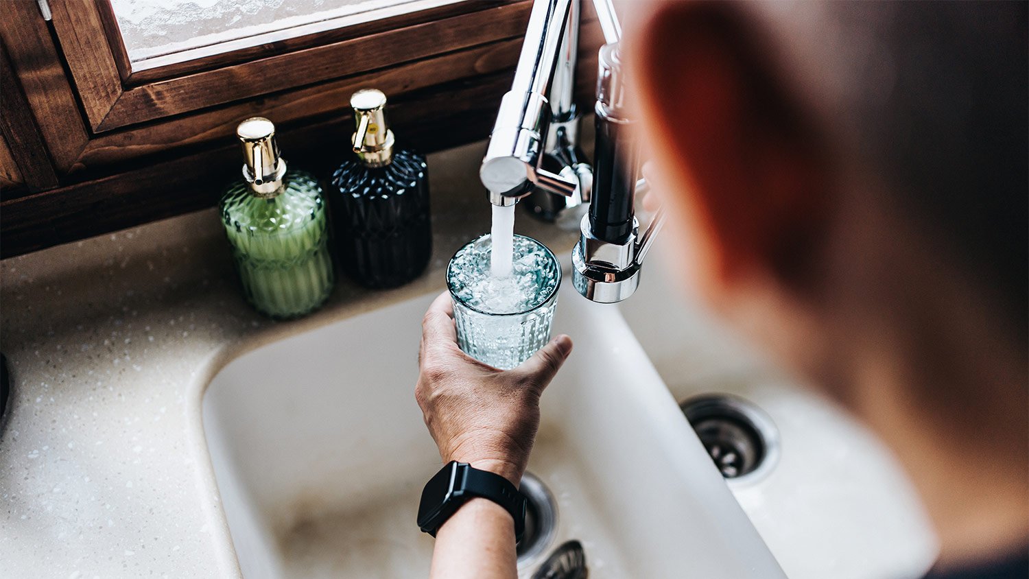 Over the shoulder view of man filling a glass from the tap in the kitchen.