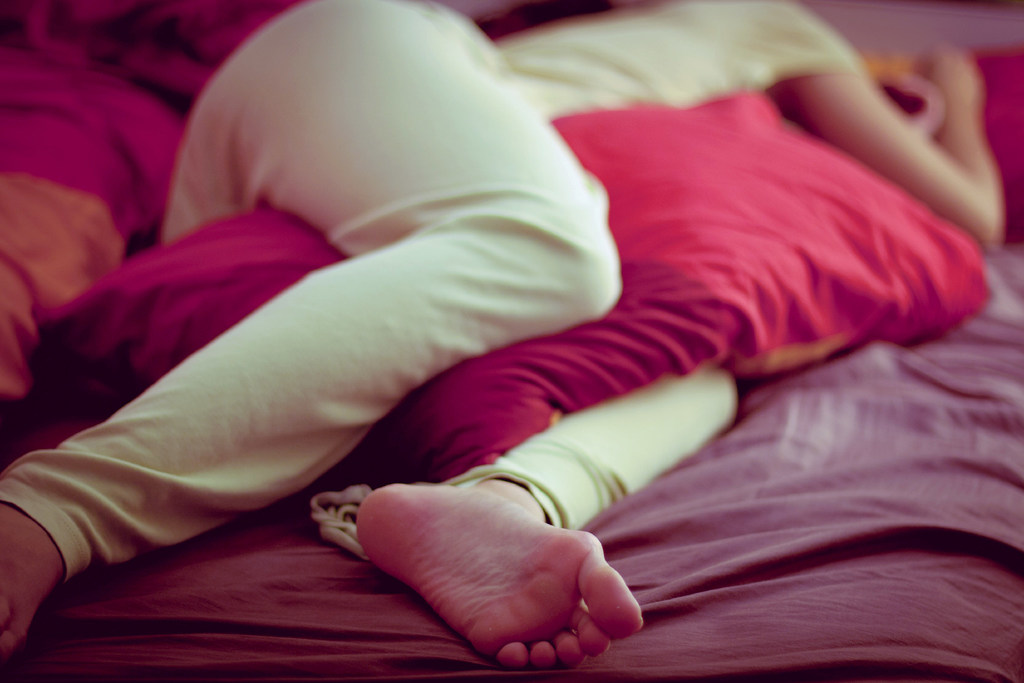 A woman sleeps with a pillow between her knees on a bed.