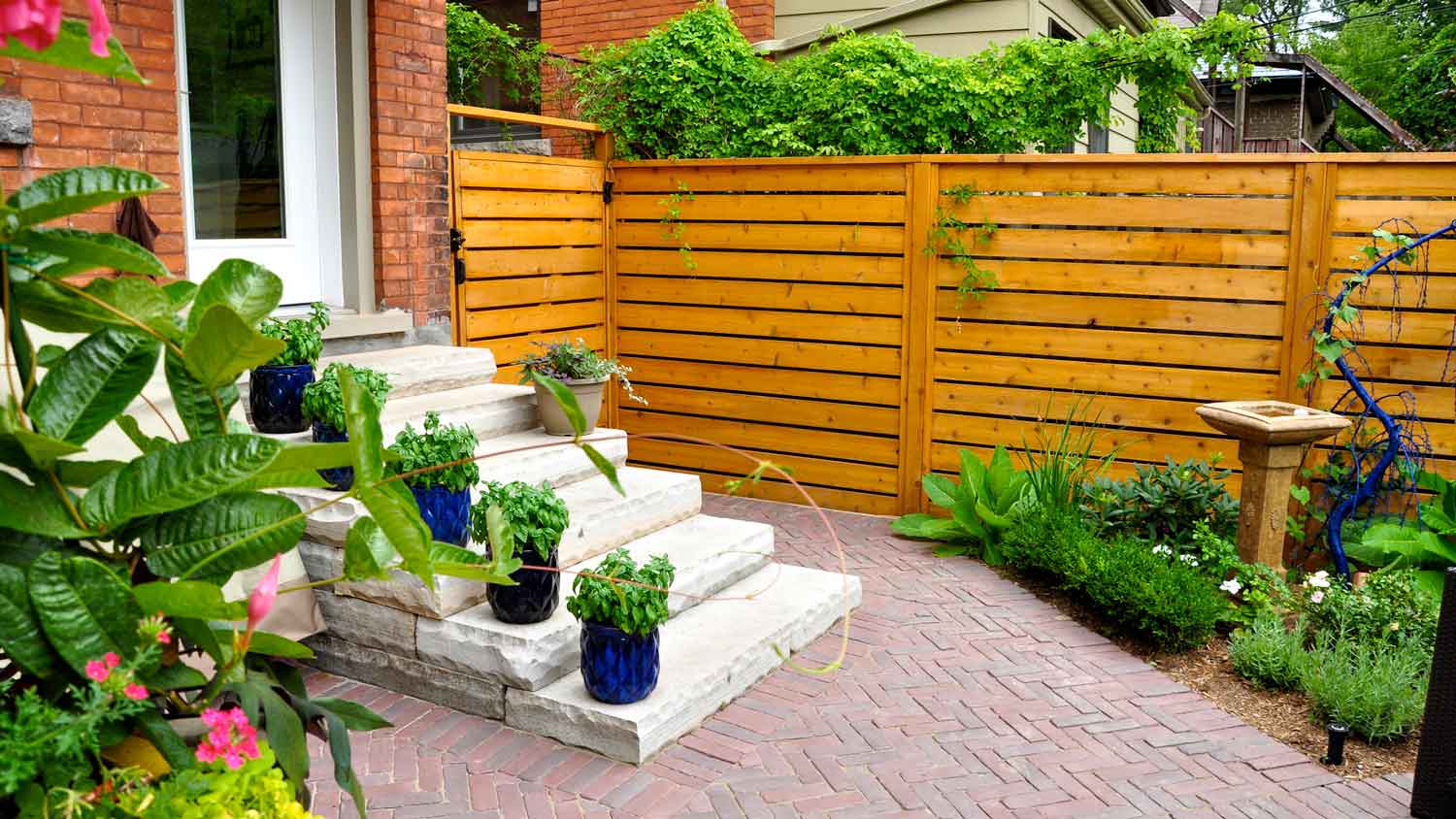 A landscaped backyard with cedar fence and herringbone patterned patio