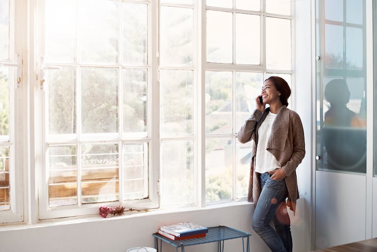 woman on phone next to large, ceiling-height windows