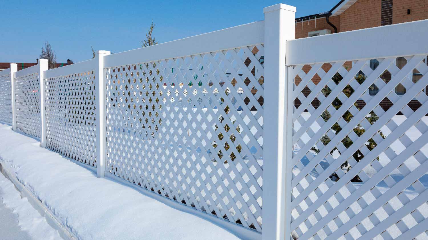 A white lattice vinyl fence on a snowy day