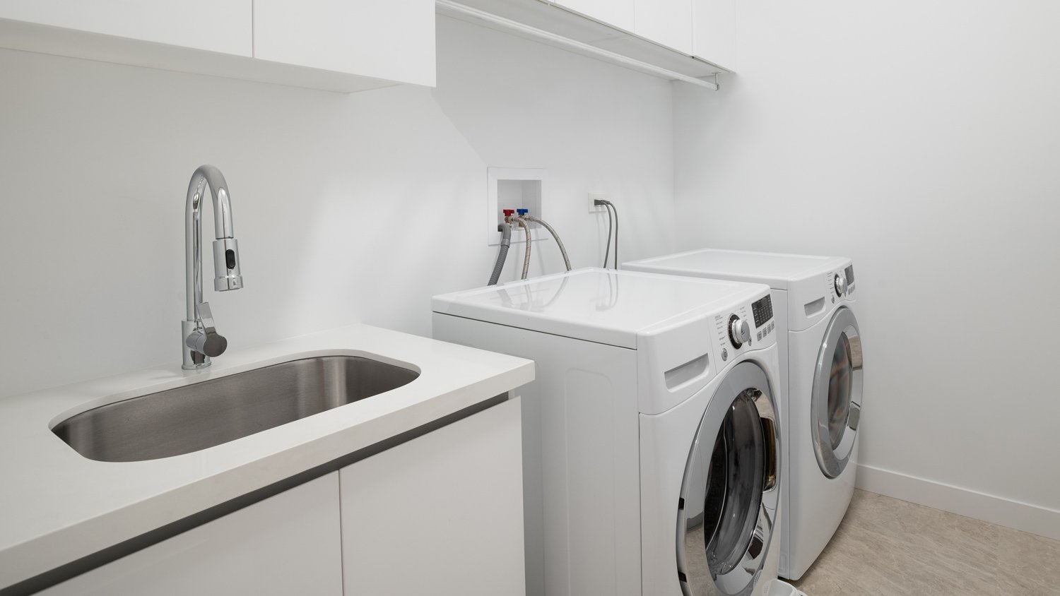 A white laundry room with a sink, white washer and dryer appliances, and a tiled floor