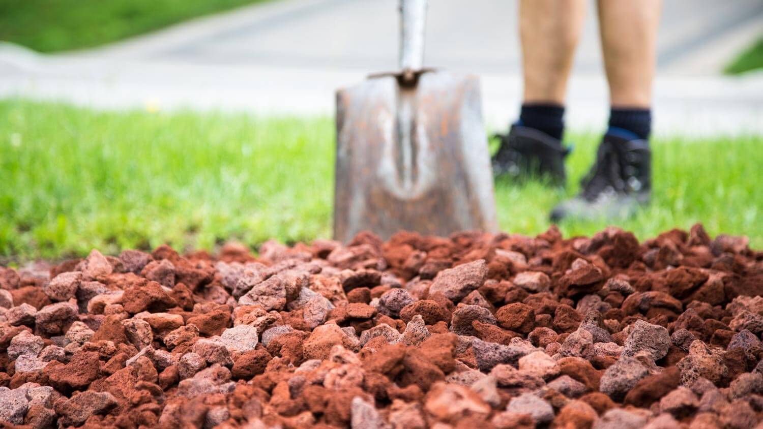 Man with shovel laying lava rocks on a garden