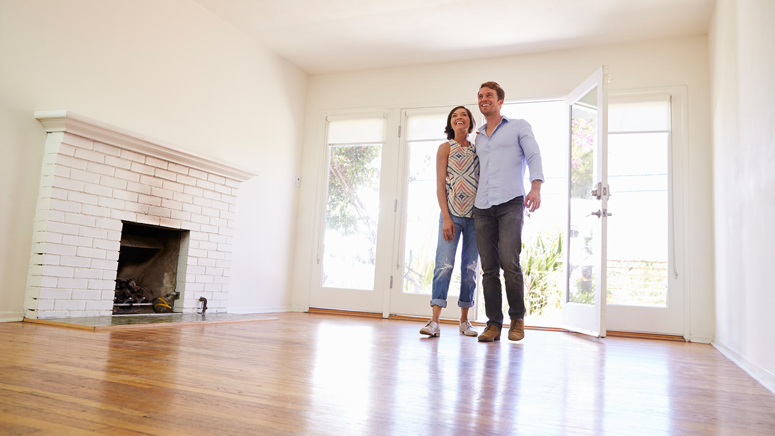 couple hugging in empty light room with wood floors 