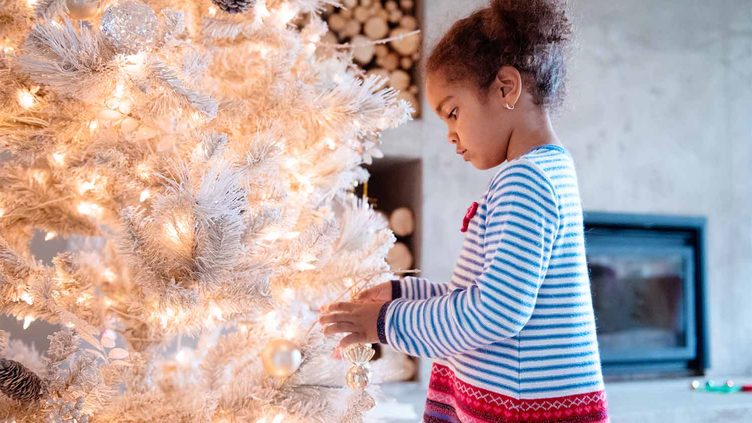 little girl putting ornaments on white christmas tree