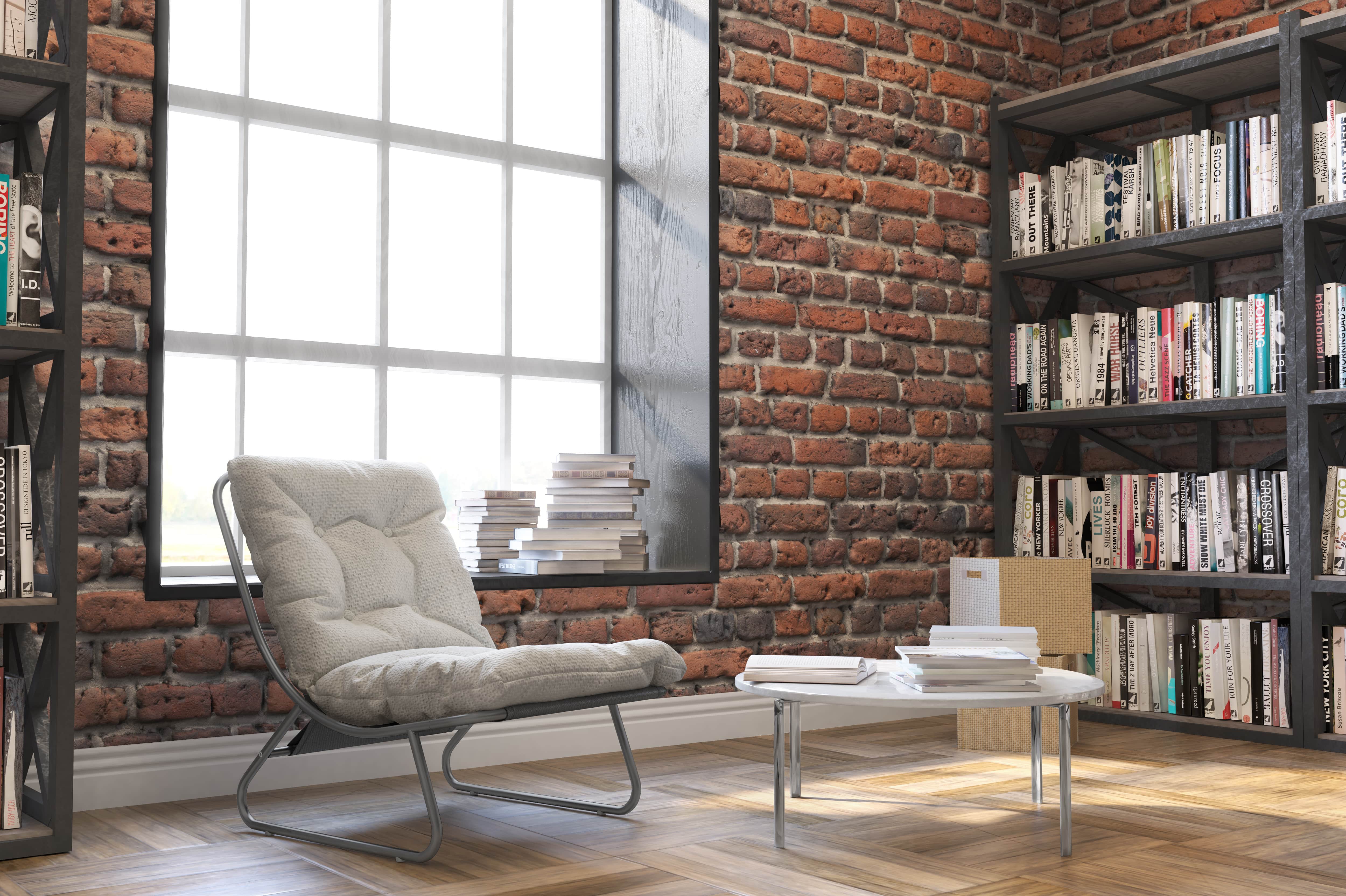 A cushioned chair in front of a large window near a book-lined bookshelf