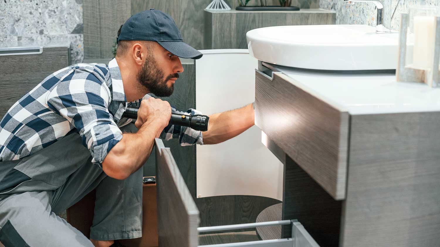 Man holding a flashlight looking under the sink