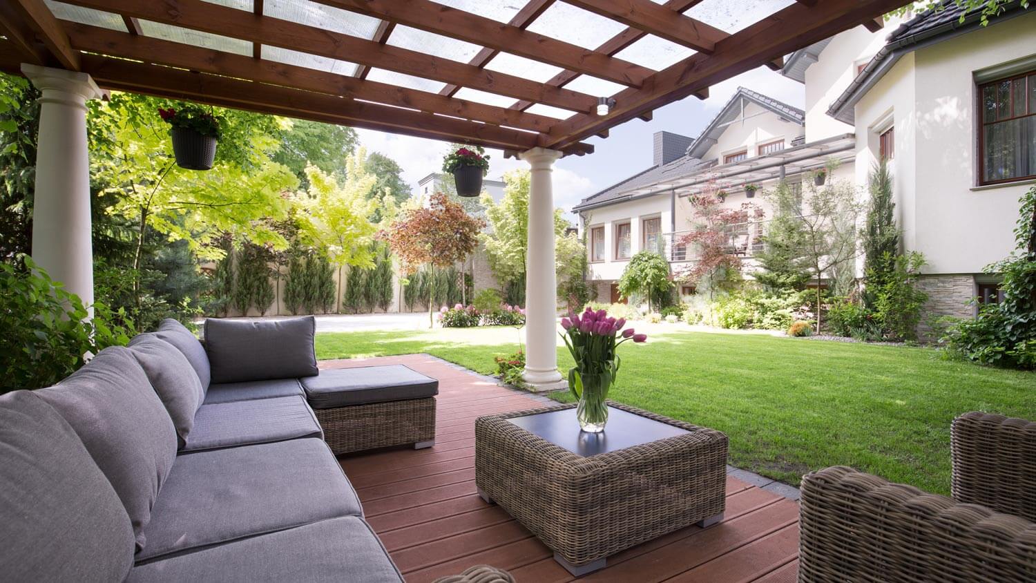 A luxurious deck with a gray sofa and a pergola providing shade