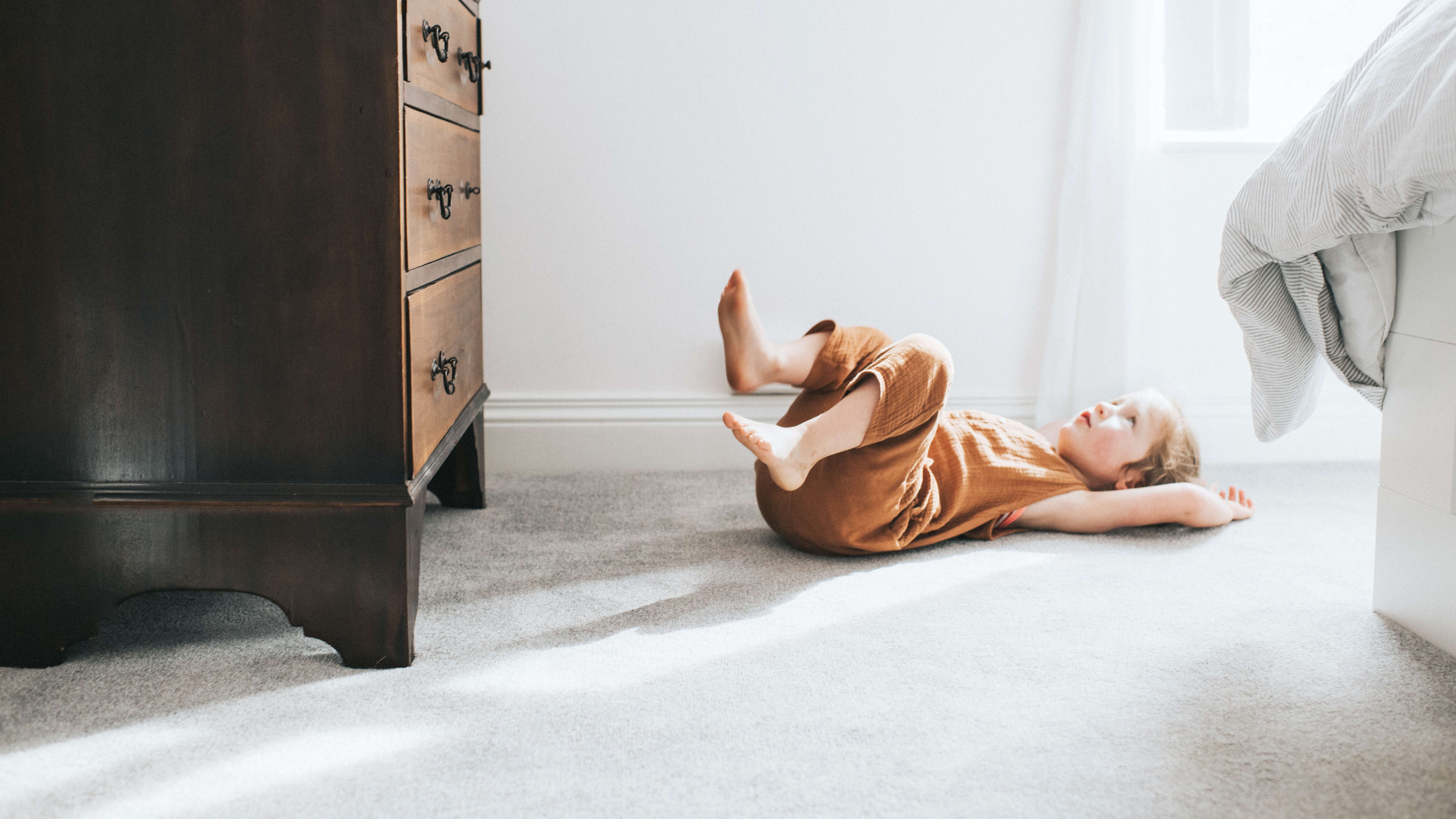 Girl lying down on a gray carpet in a bright bedroom