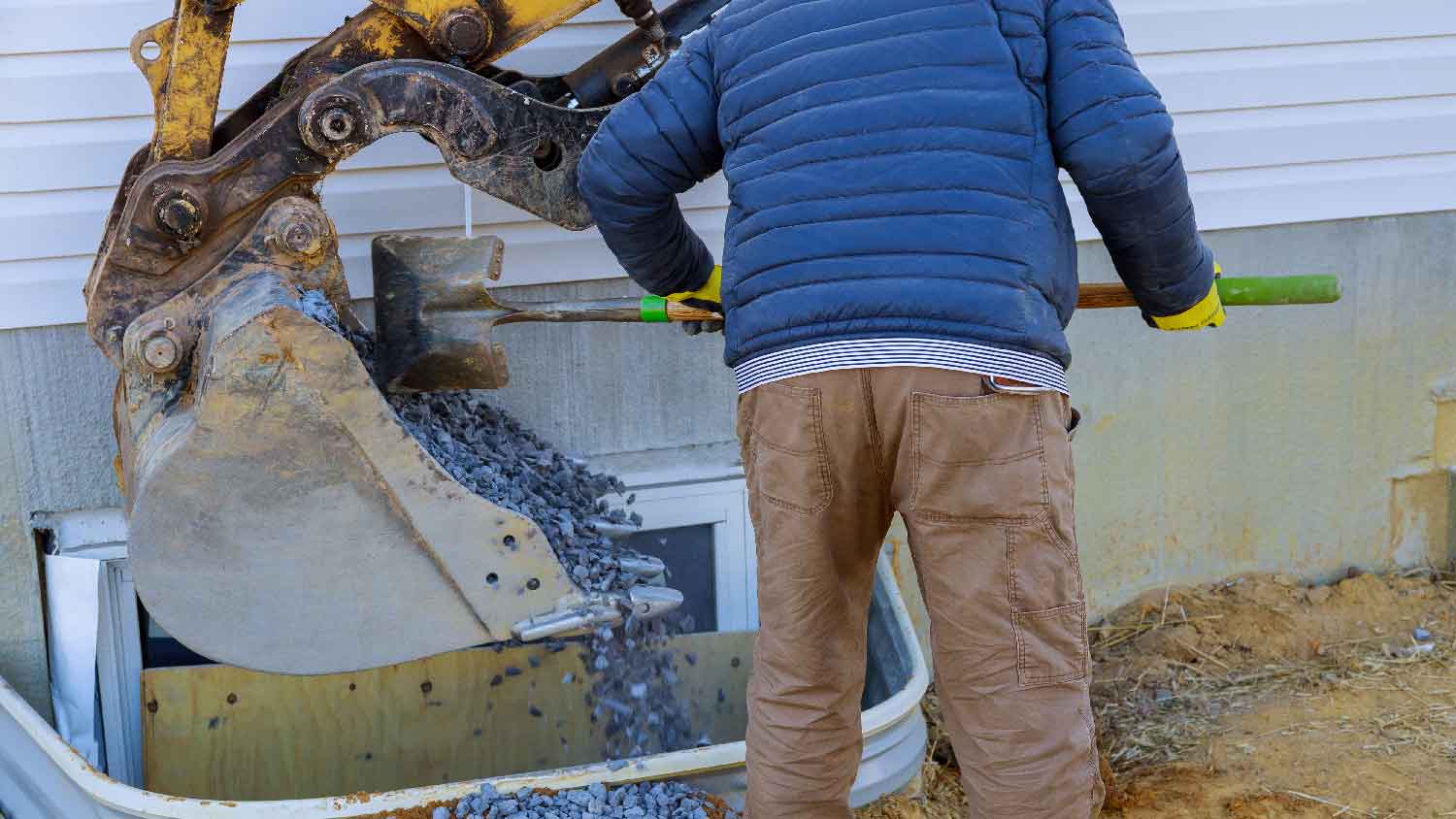 A man adding gravel with shovel to a window well 