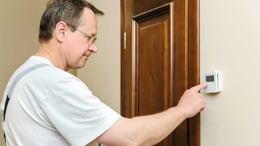 Man adjusting temperature on a thermostat mounted on the wall 