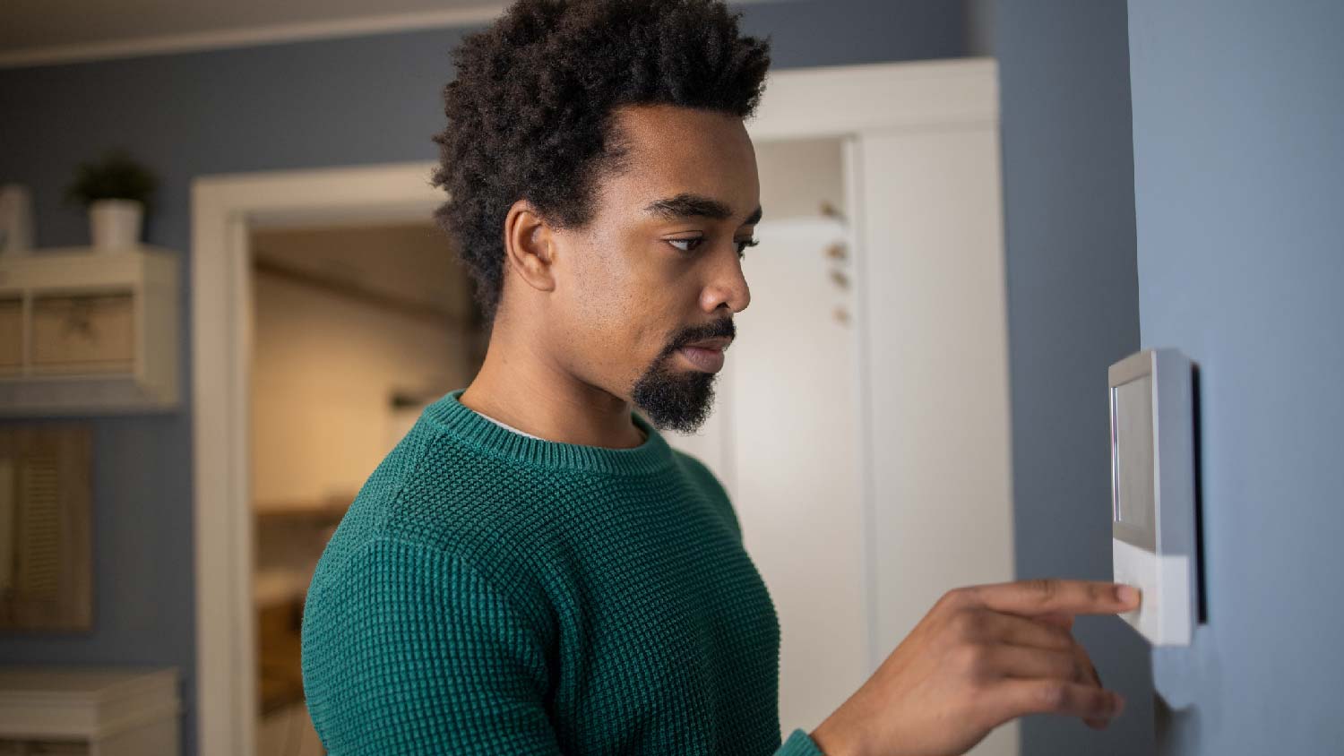 A man adjusting the temperature via a thermostat