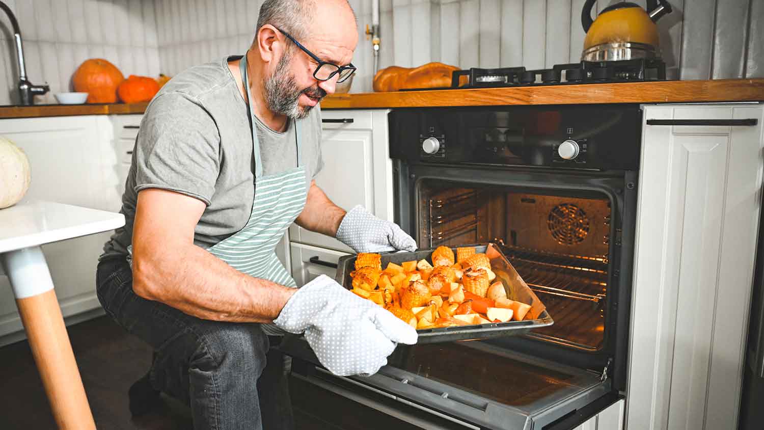 A man taking roasted vegetables out of the oven.