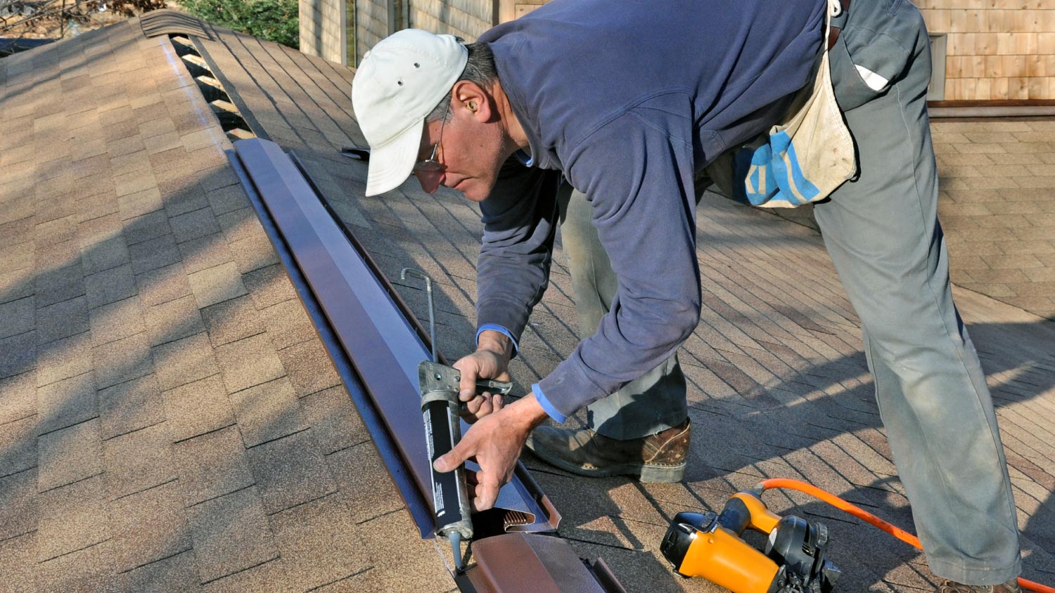 A man caulking ridge vent